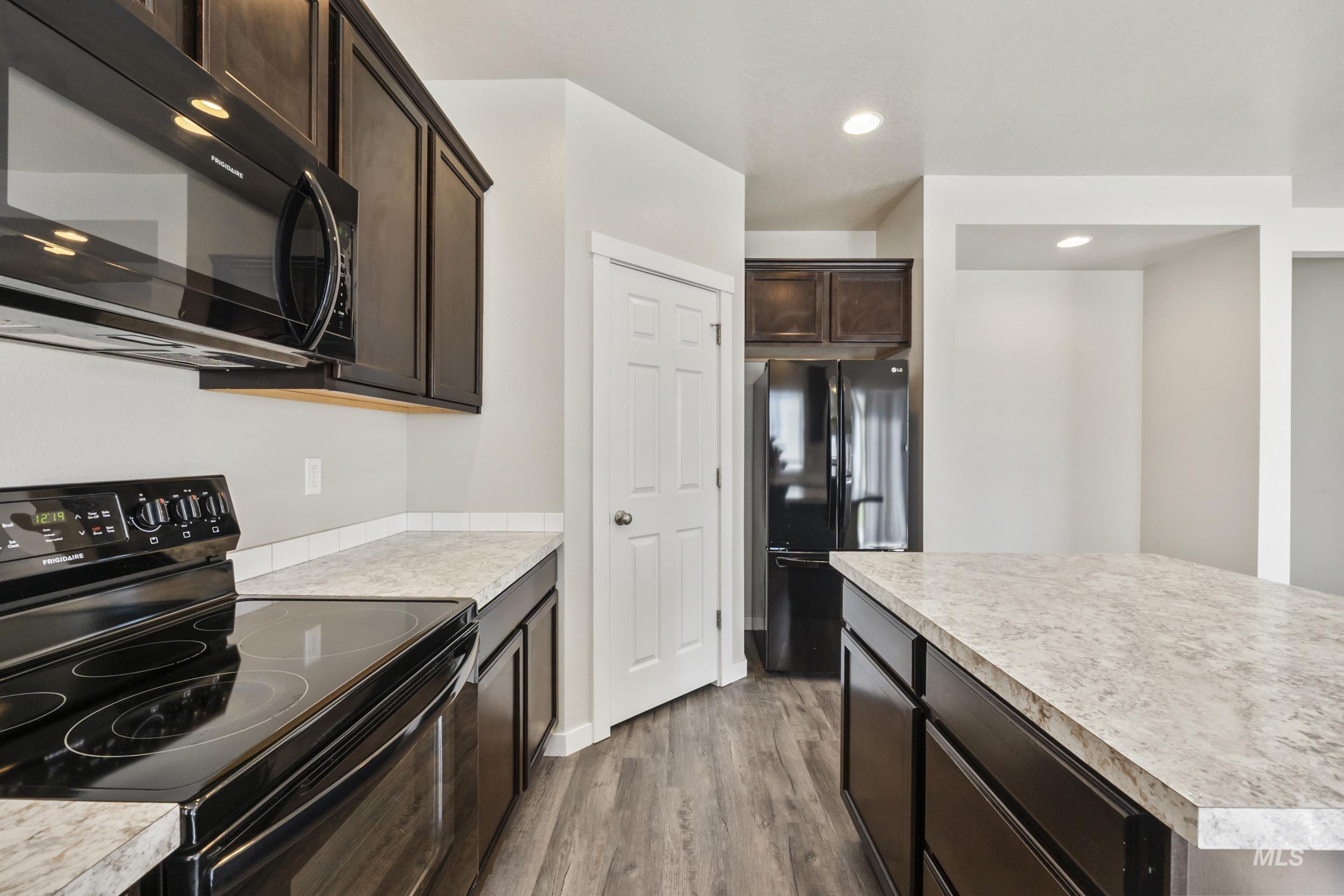 Kitchen featuring black appliances, dark brown cabinetry, dark wood-style flooring, light countertops, and recessed lighting