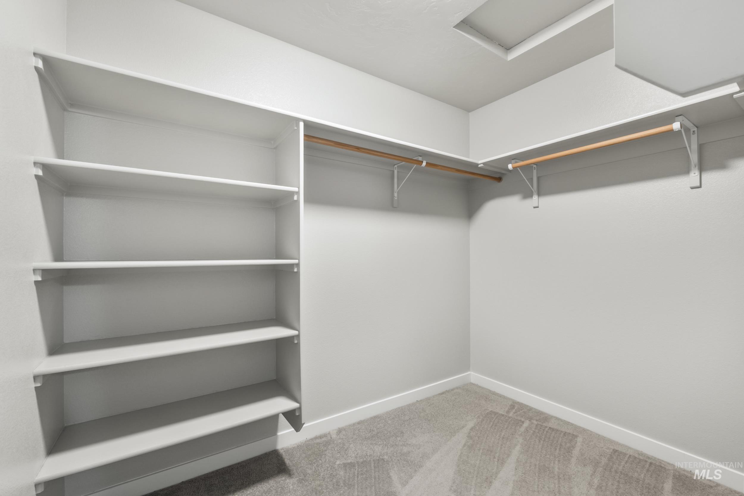 Walk in closet with light carpet and attic access