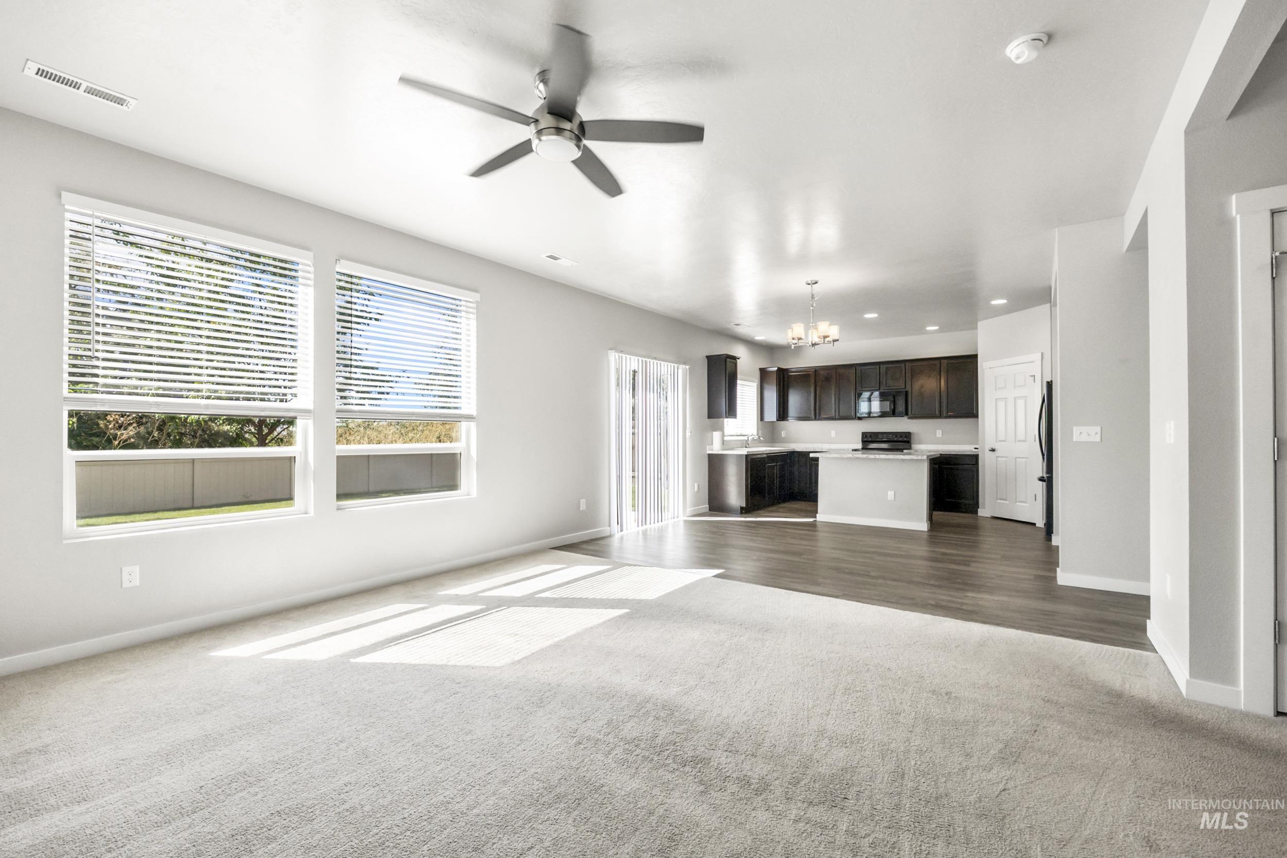 Unfurnished living room featuring dark colored carpet, a chandelier, a ceiling fan, and recessed lighting