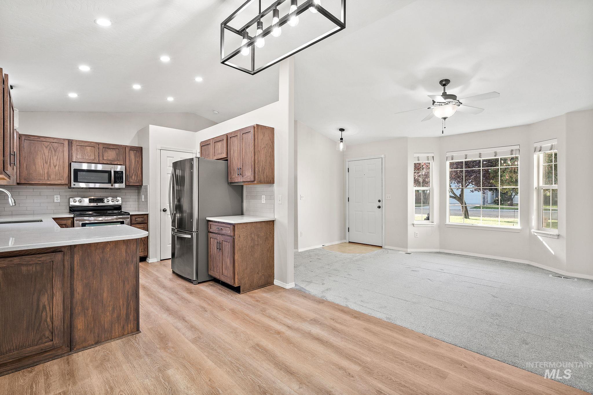 Kitchen featuring vaulted ceiling, tasteful backsplash, appliances with stainless steel finishes, open floor plan, and a peninsula