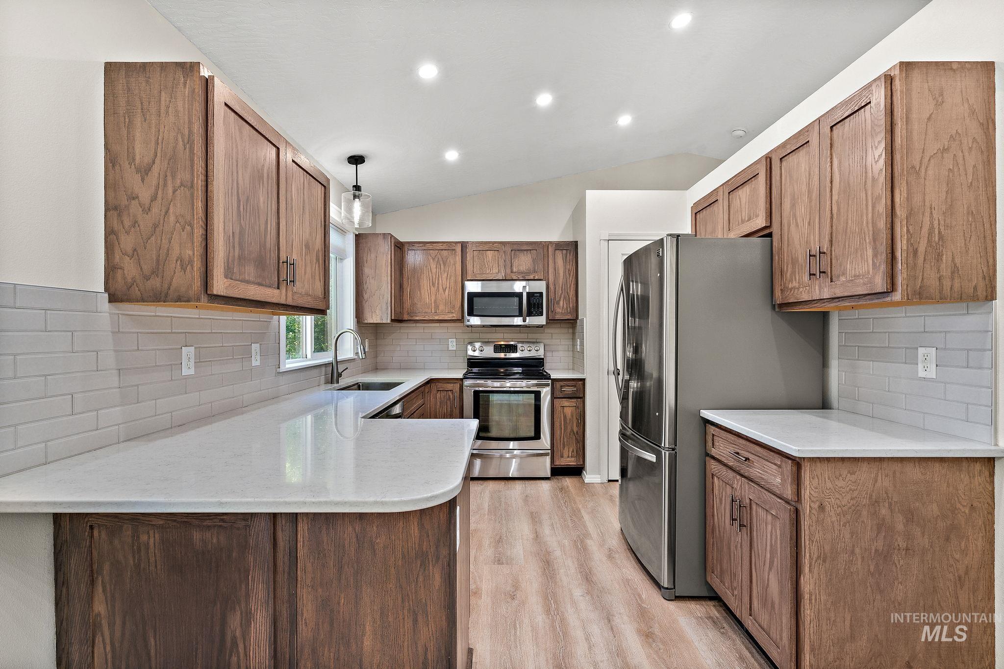 Kitchen featuring backsplash, stainless steel appliances, decorative light fixtures, vaulted ceiling, and a peninsula