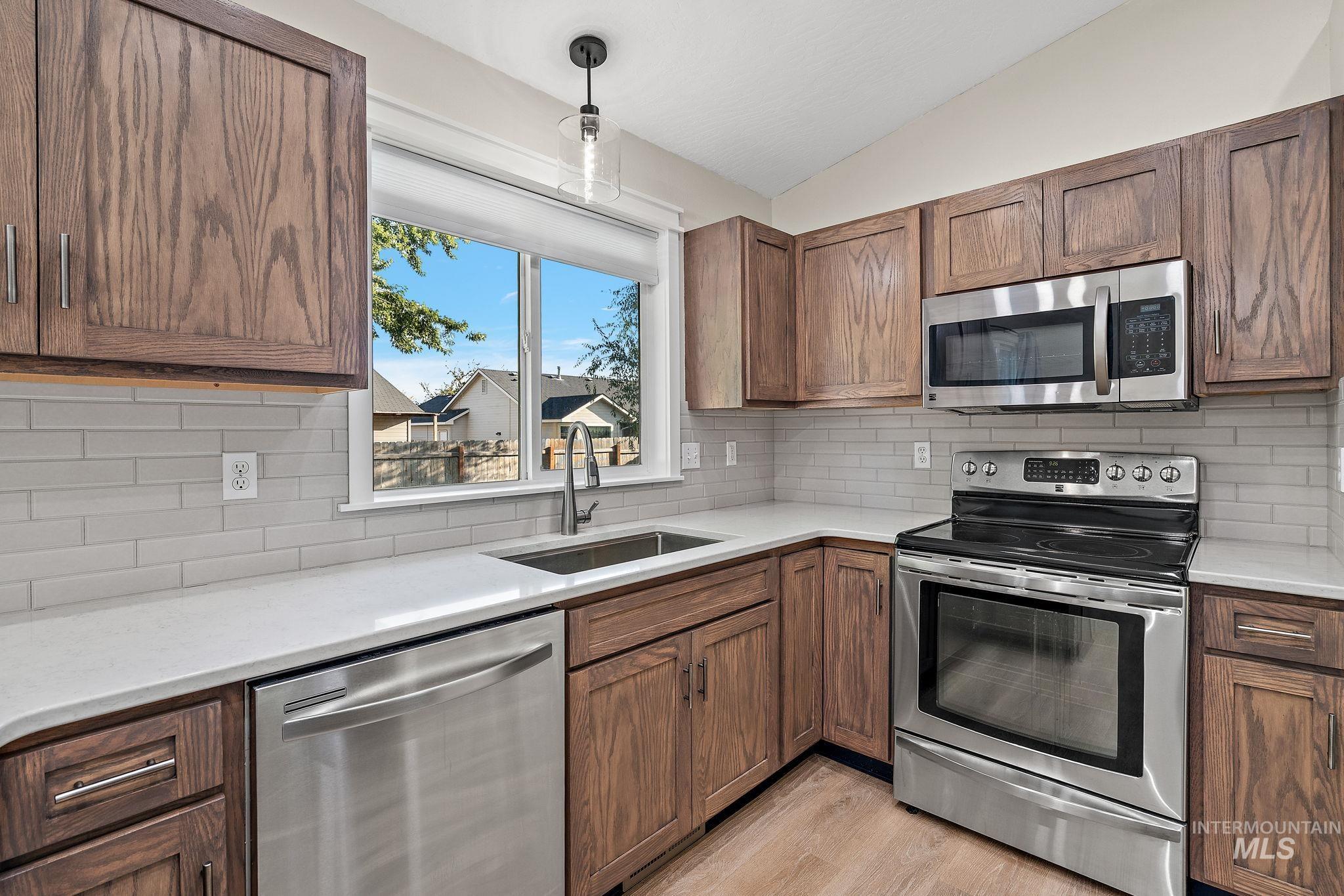 Kitchen with stainless steel appliances, lofted ceiling, pendant lighting, tasteful backsplash, and light wood-style flooring