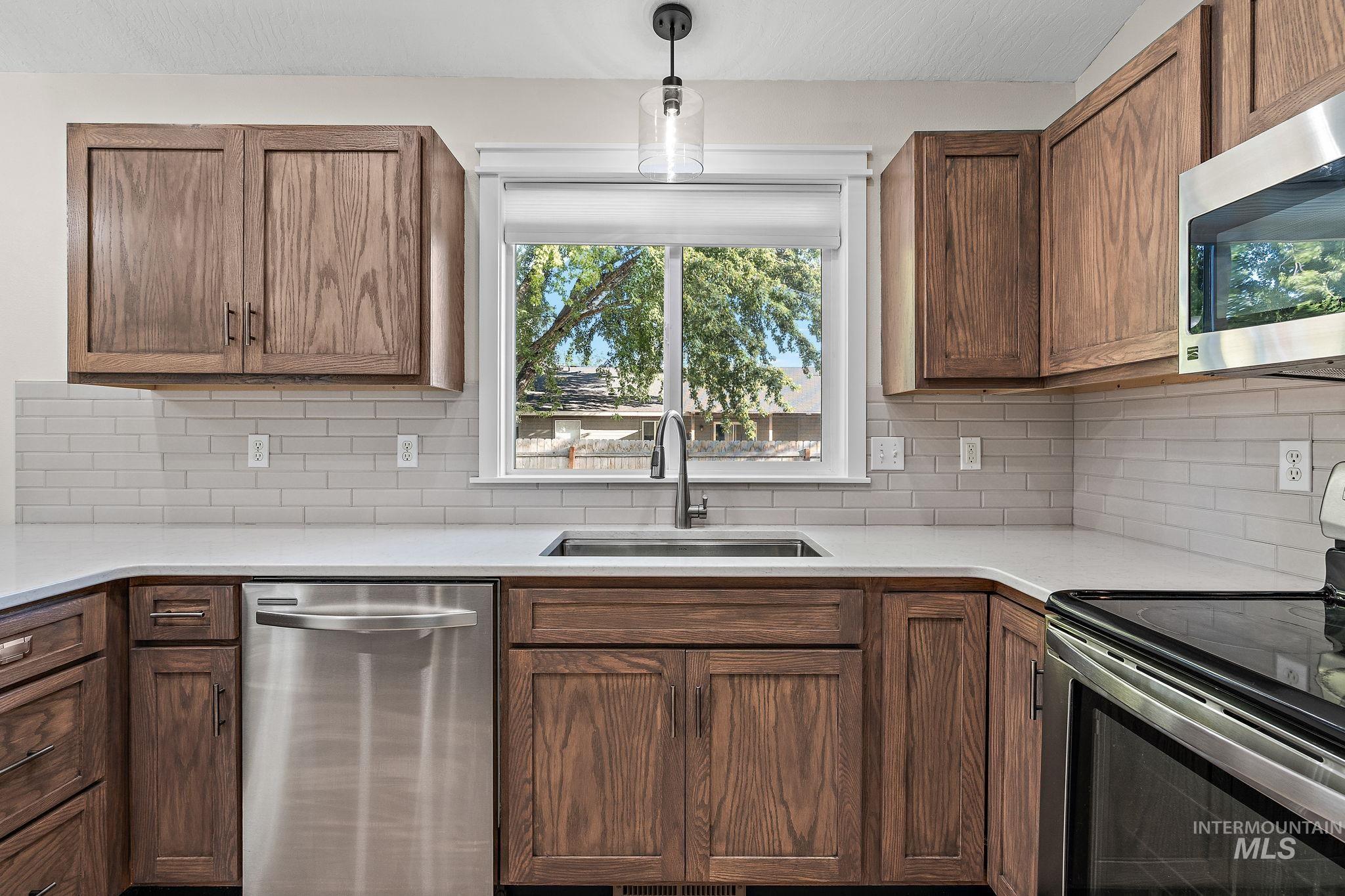 Kitchen featuring stainless steel appliances, plenty of natural light, decorative light fixtures, and brown cabinetry