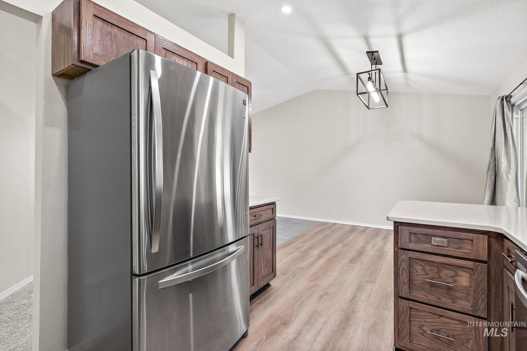 Kitchen with freestanding refrigerator, vaulted ceiling, light wood-style floors, dark brown cabinetry, and pendant lighting