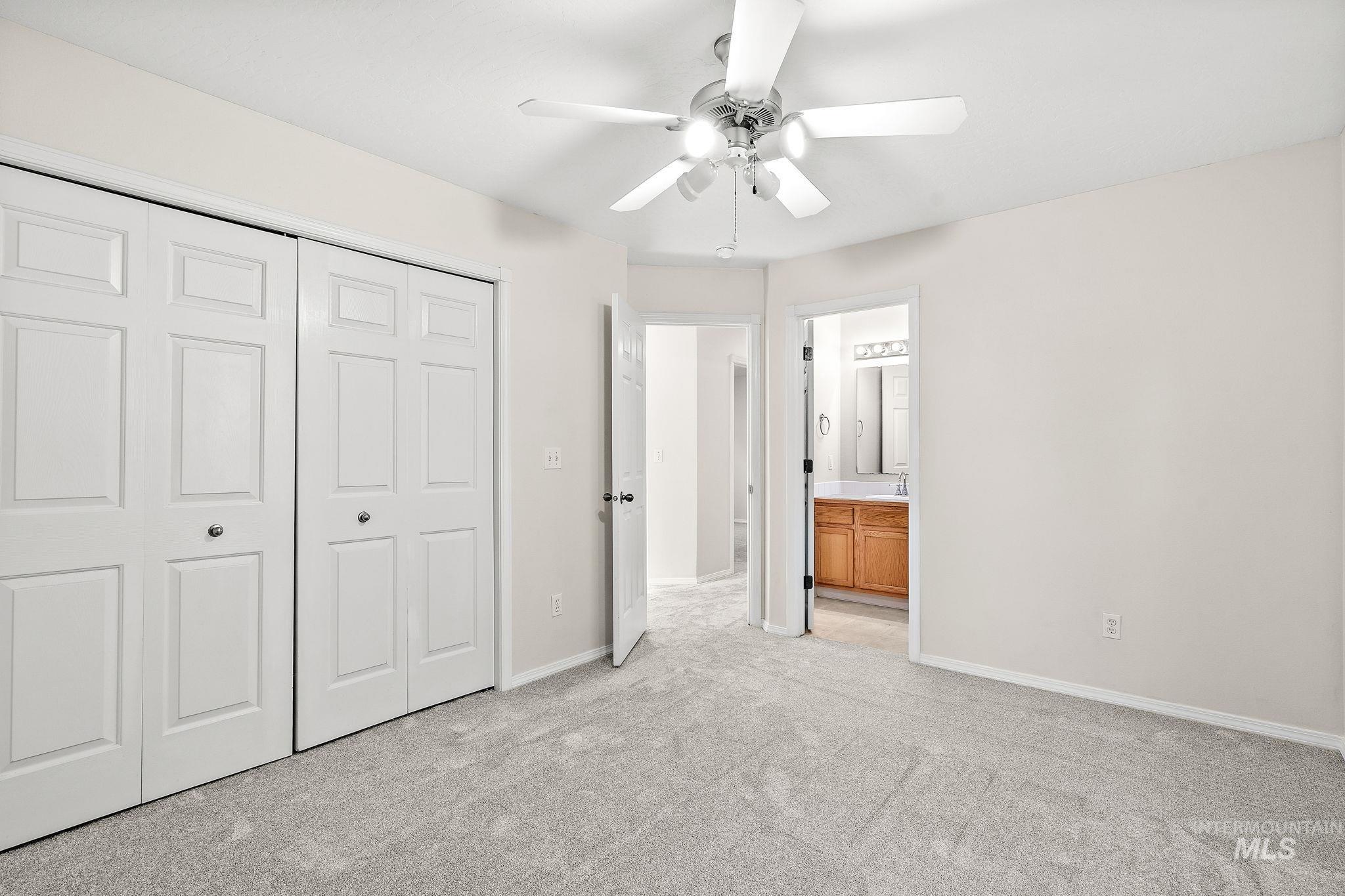 Unfurnished bedroom with light carpet, a closet, ceiling fan, and ensuite bathroom