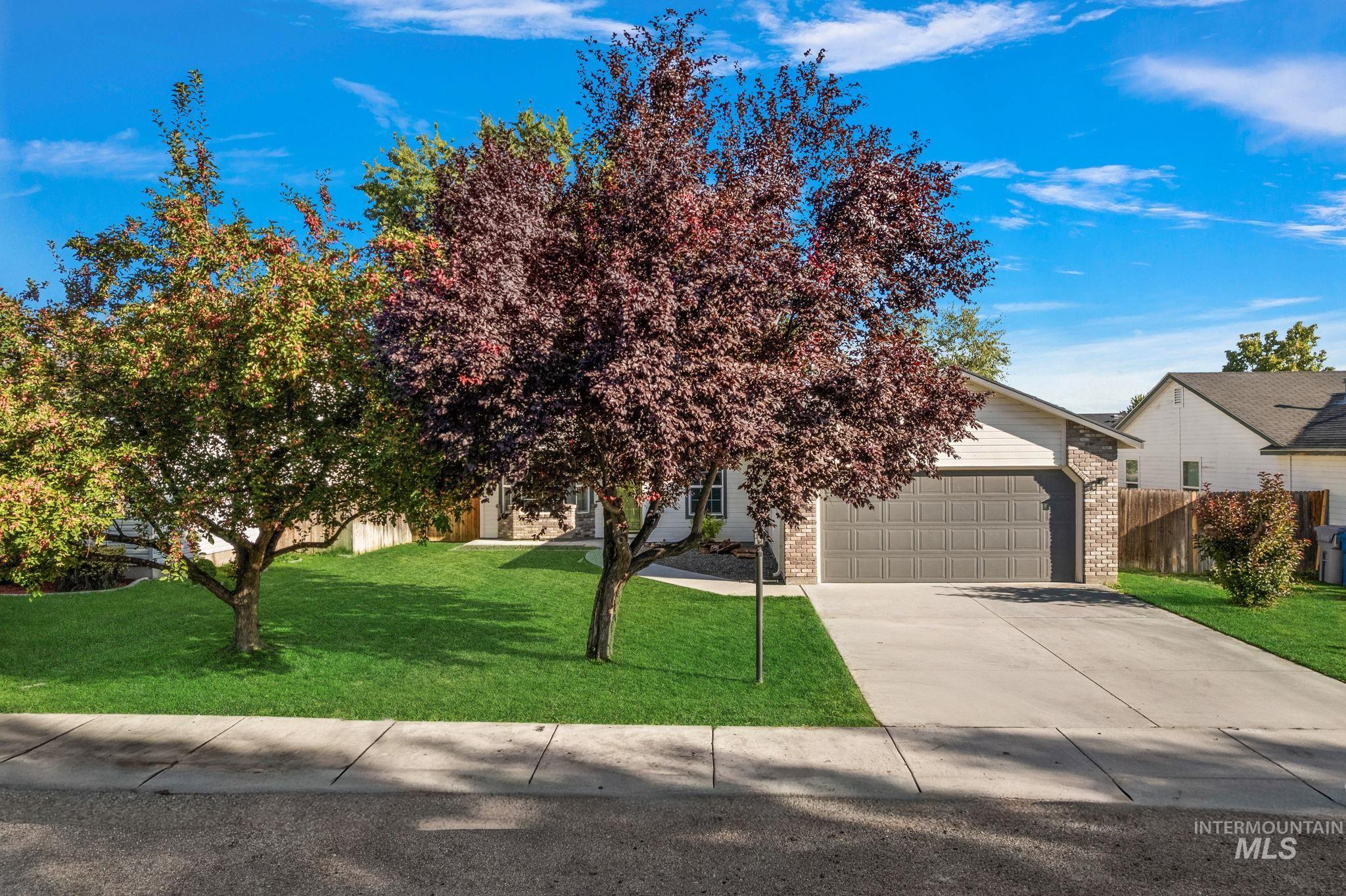 View of property hidden behind natural elements featuring brick siding, concrete driveway, and a garage