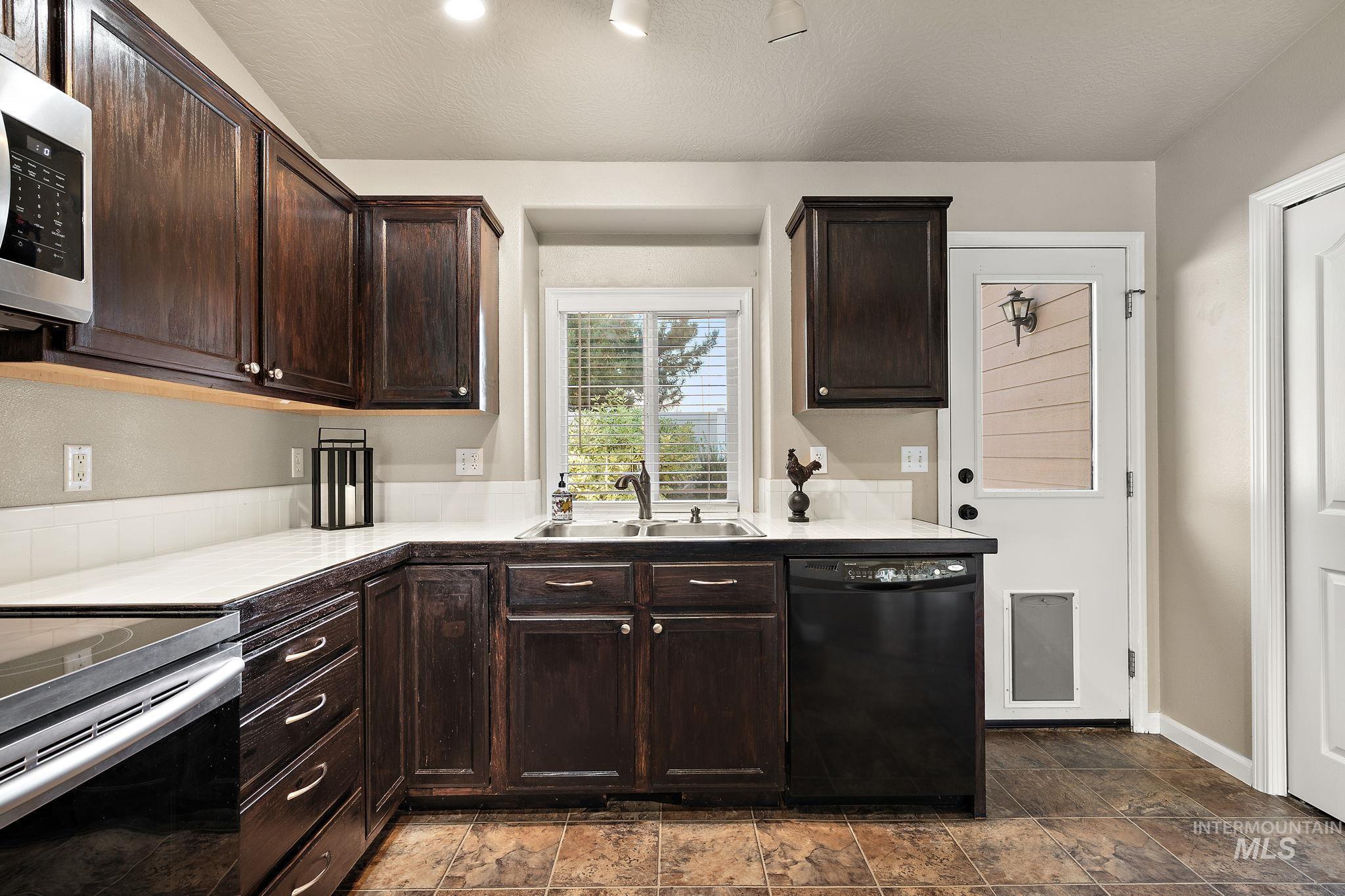 Kitchen featuring black dishwasher, dark brown cabinetry, stainless steel microwave, tile counters, and a textured ceiling