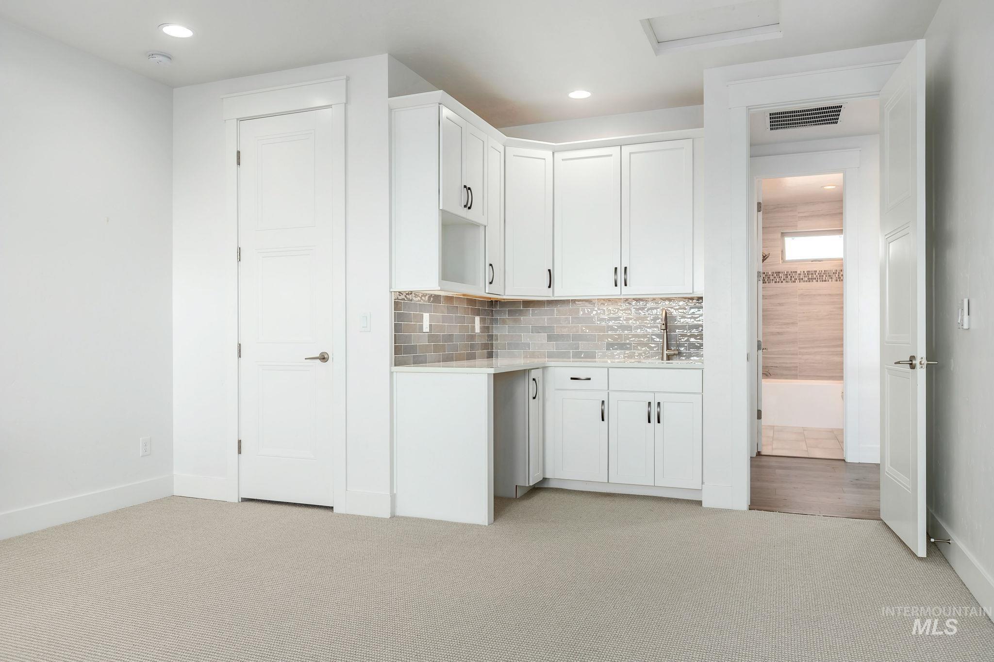 Bar area featuring decorative backsplash, white cabinets, light carpet, recessed lighting, and light stone counters