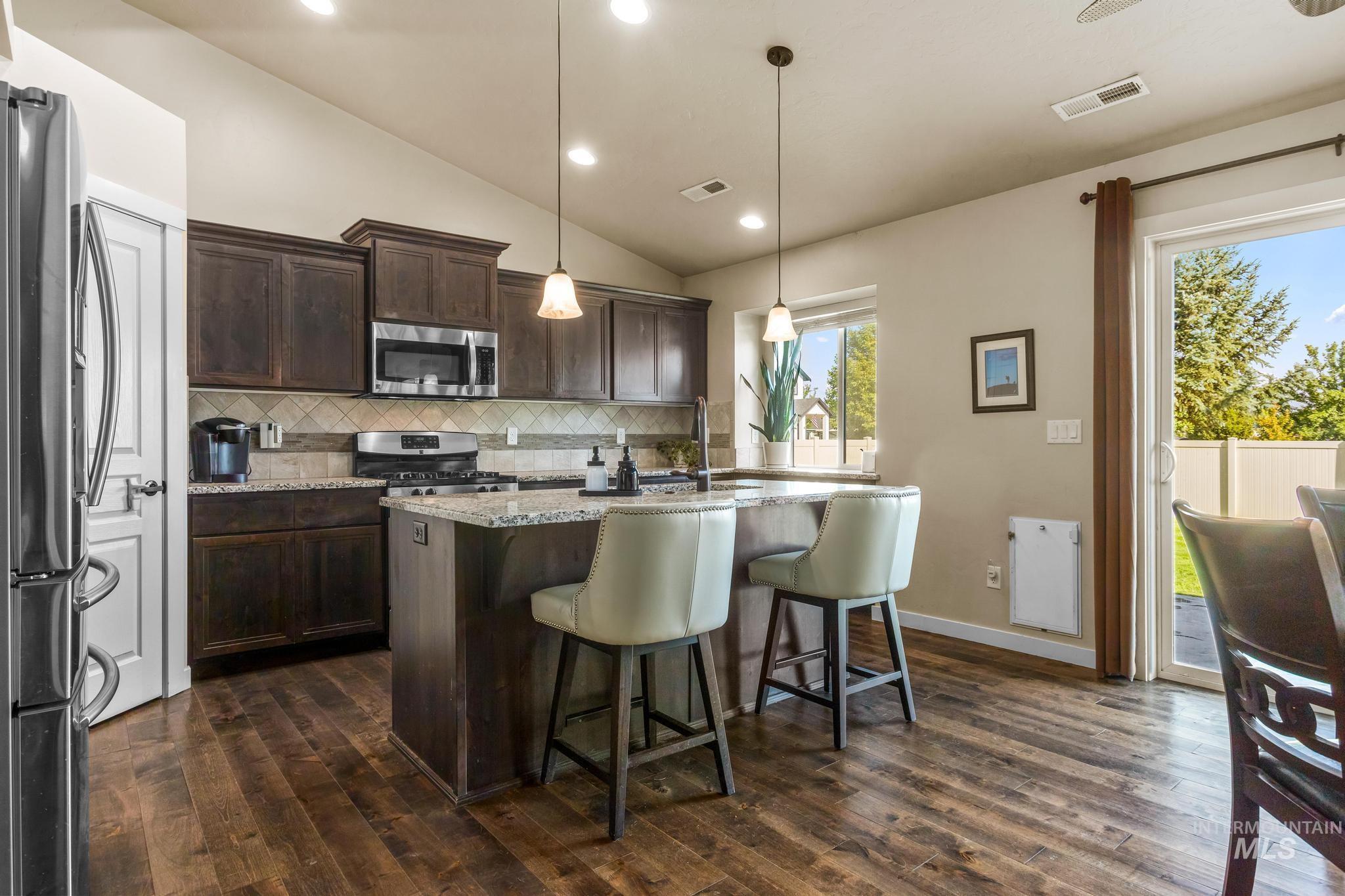 Kitchen with light stone countertops, dark brown cabinets, vaulted ceiling, stainless steel appliances, and backsplash
