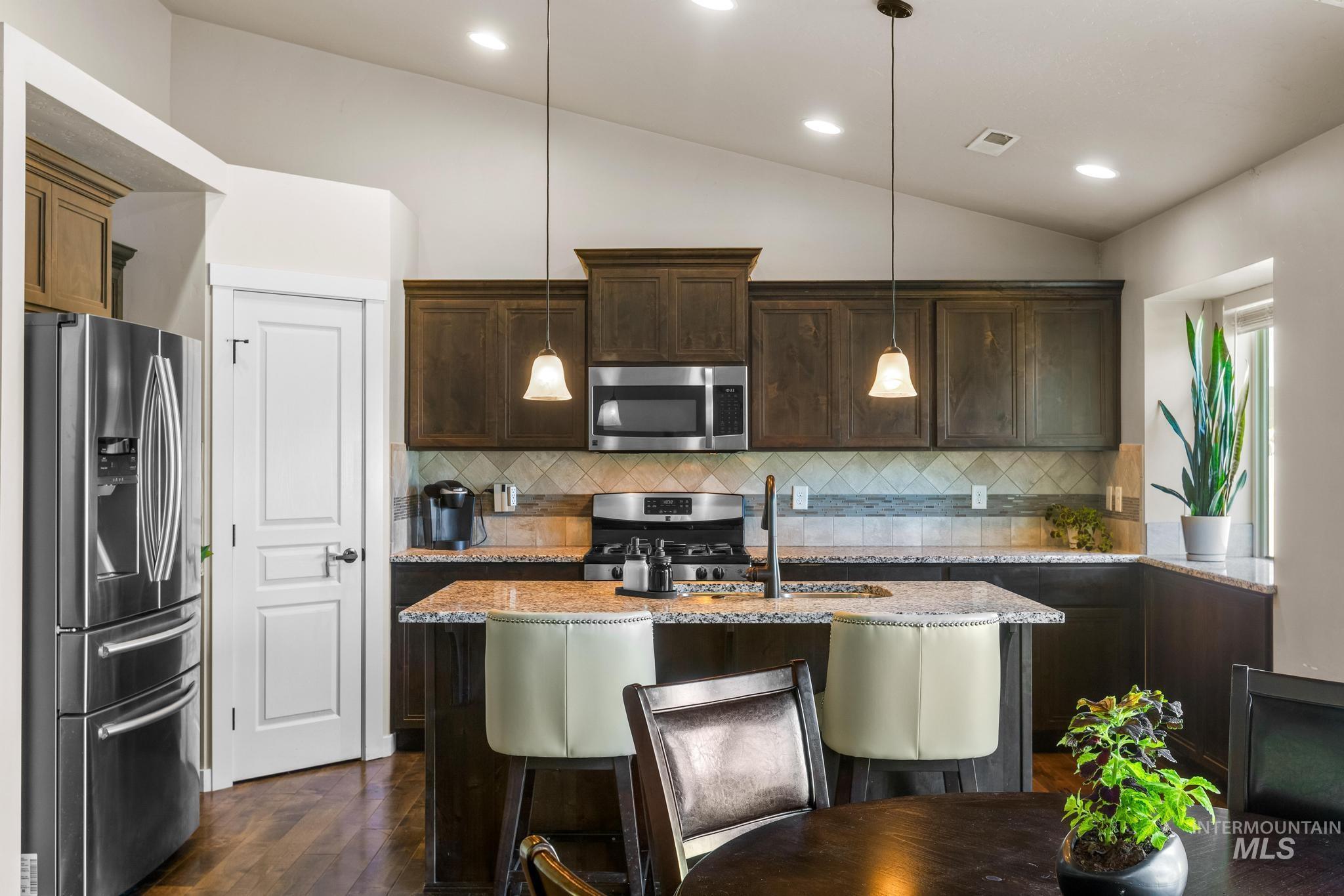 Kitchen with appliances with stainless steel finishes, a kitchen breakfast bar, lofted ceiling, light stone counters, and dark brown cabinetry