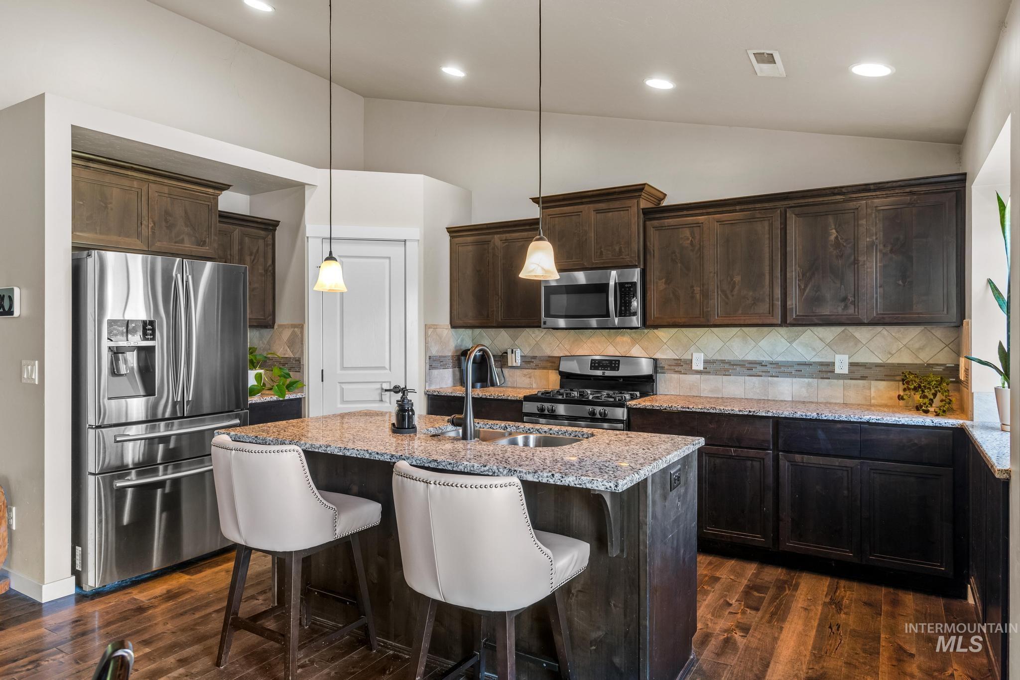 Kitchen featuring dark brown cabinetry, lofted ceiling, appliances with stainless steel finishes, backsplash, and light stone counters