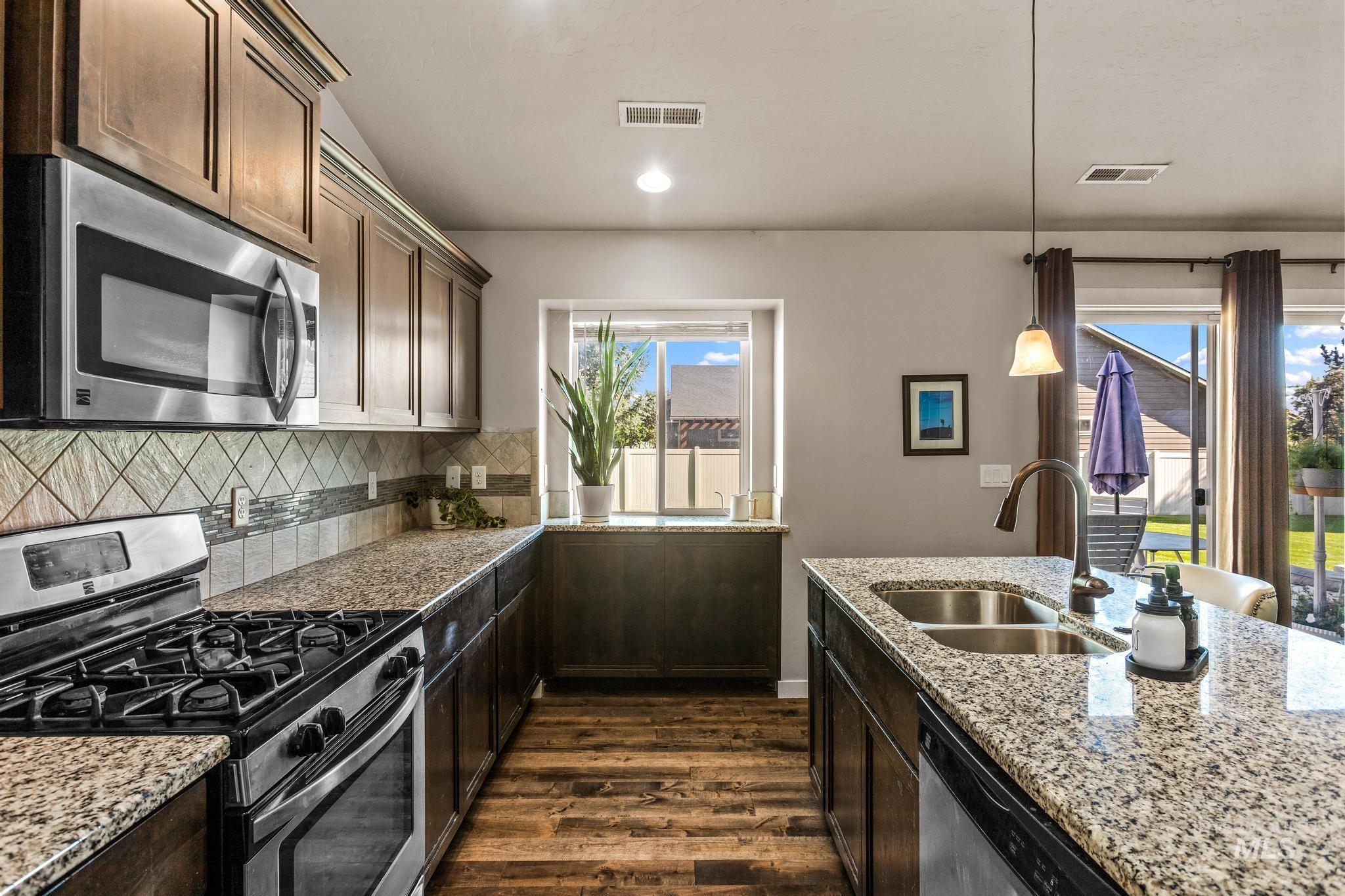 Kitchen featuring appliances with stainless steel finishes, dark wood-type flooring, dark brown cabinets, backsplash, and pendant lighting