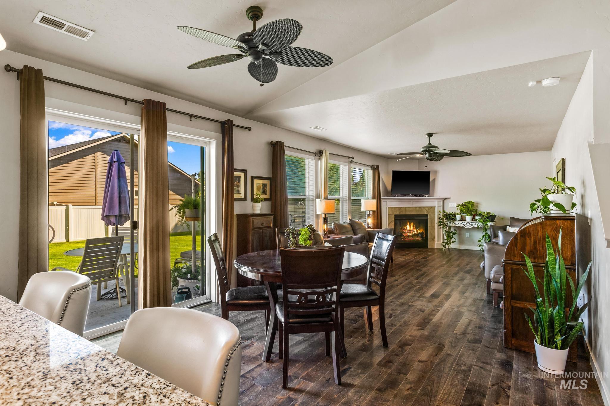 Dining space with a tile fireplace, dark wood-type flooring, lofted ceiling, and ceiling fan