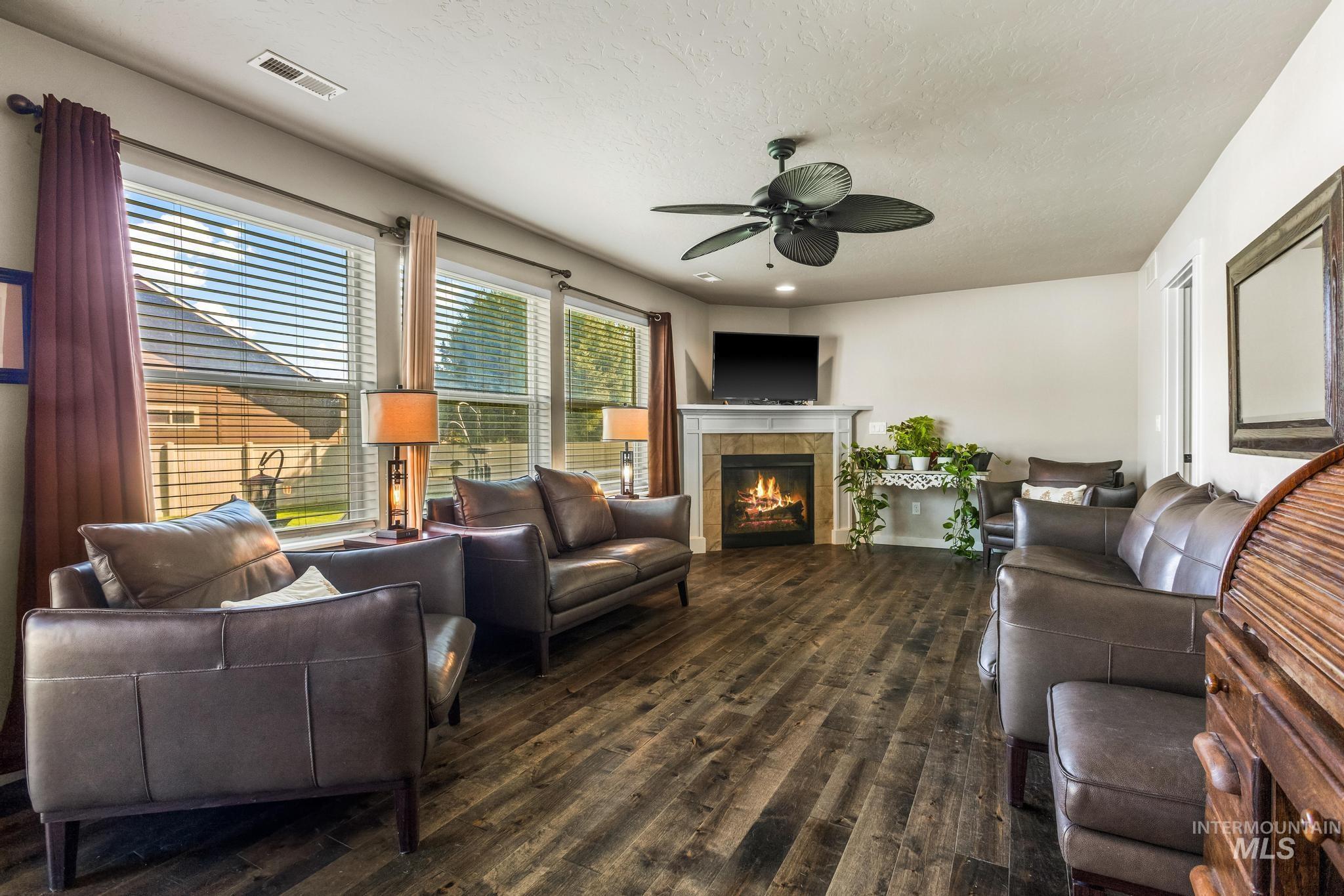 Living room with a textured ceiling, a tiled fireplace, dark wood-style floors, ceiling fan, and recessed lighting