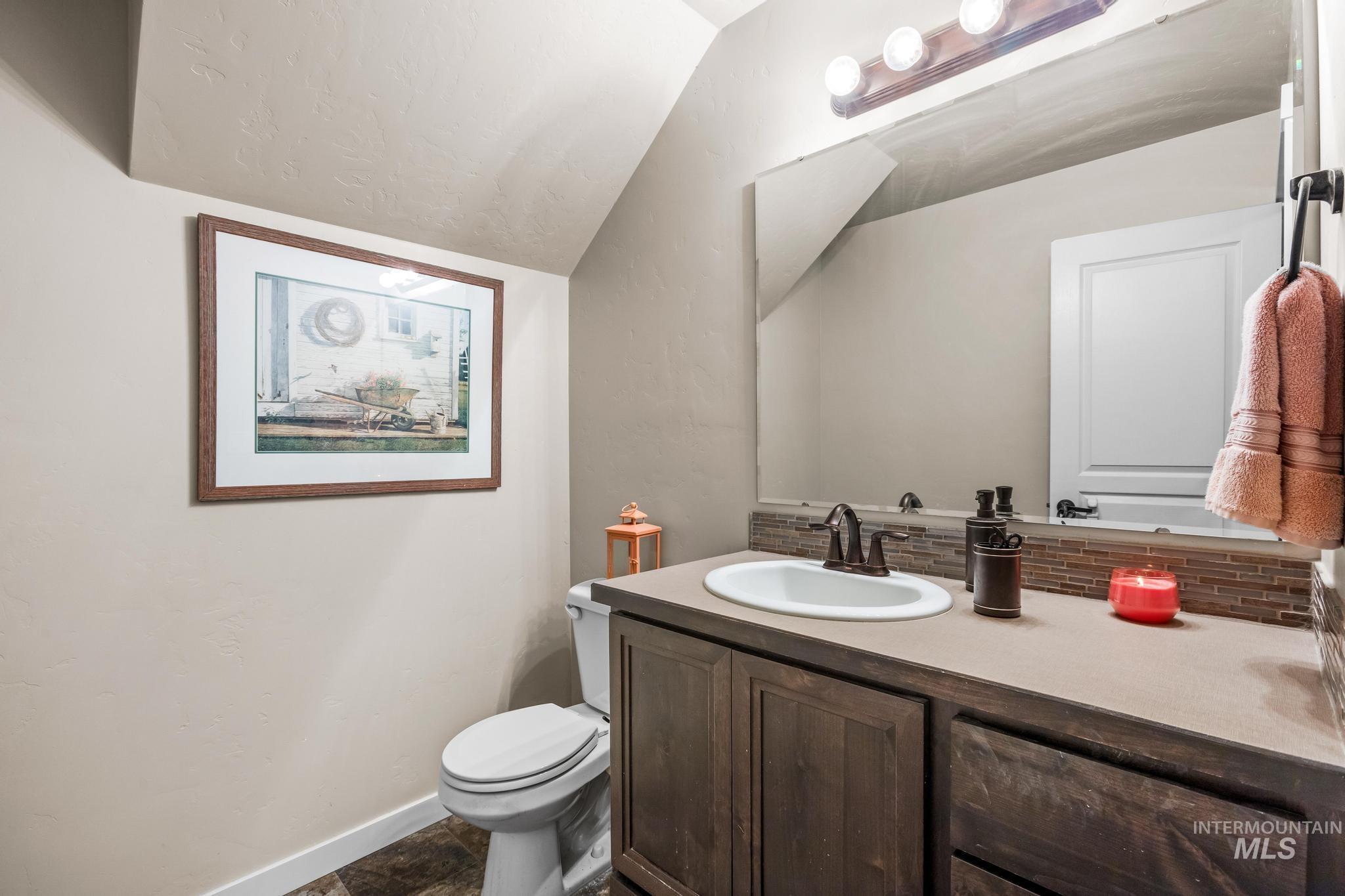 Bathroom with vanity, backsplash, vaulted ceiling, and dark stone finish floors