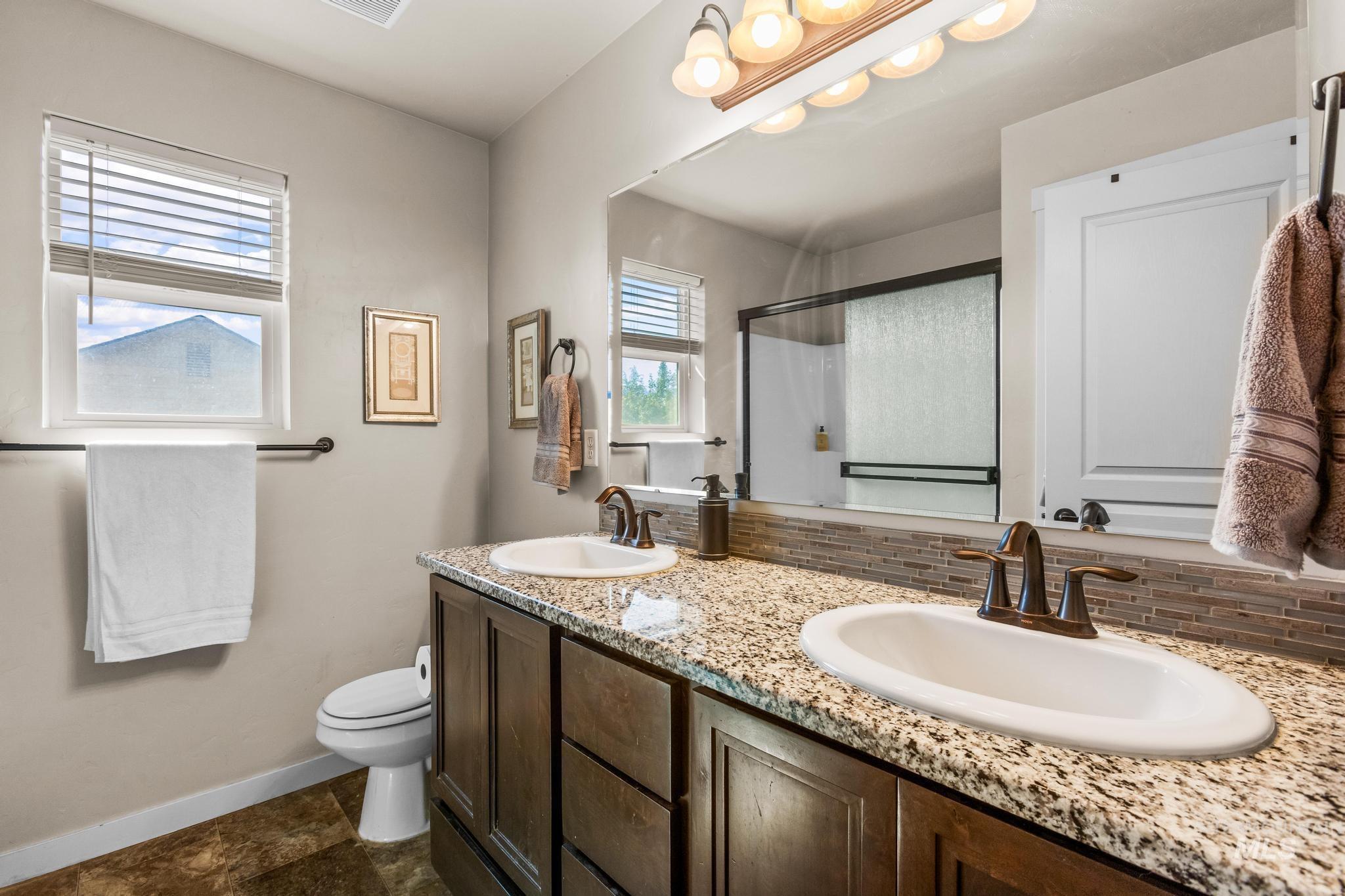 Bathroom featuring a stall shower, double vanity, tasteful backsplash, and dark stone finish floors