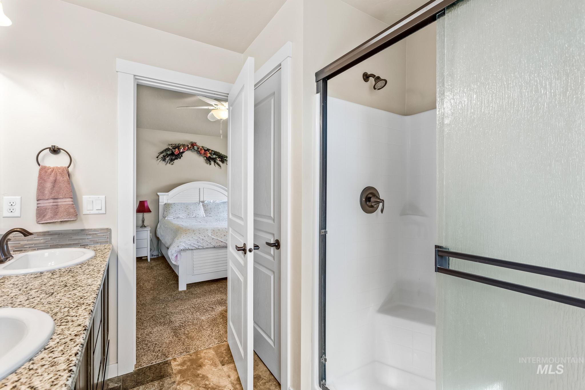 Full bathroom featuring a stall shower, double vanity, ensuite bathroom, and a ceiling fan