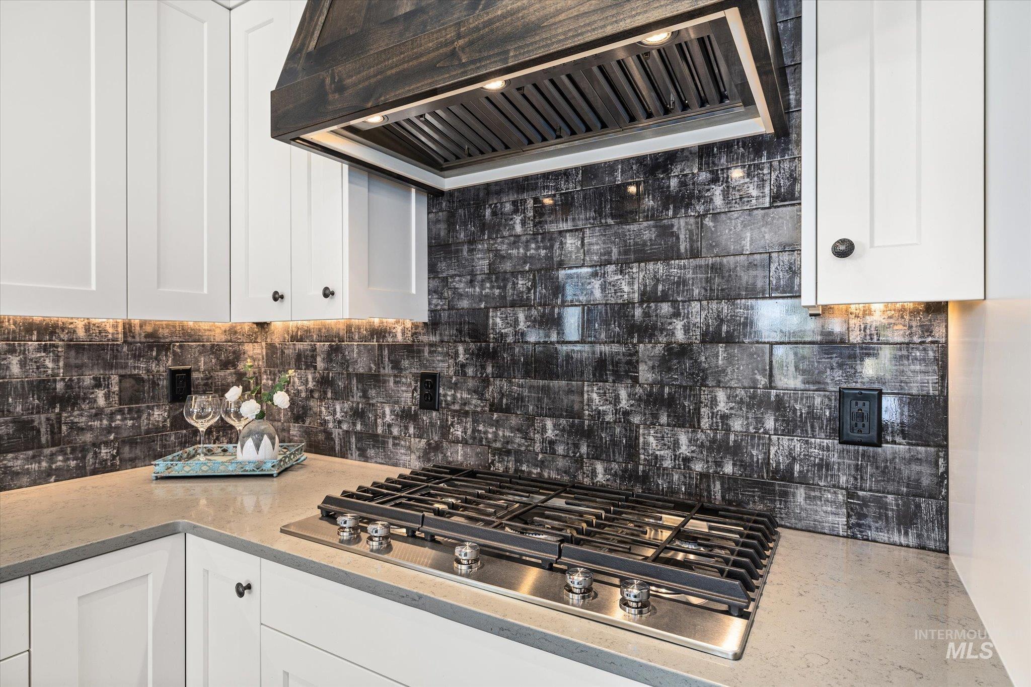 Kitchen featuring premium range hood, stainless steel gas cooktop, decorative backsplash, and white cabinetry