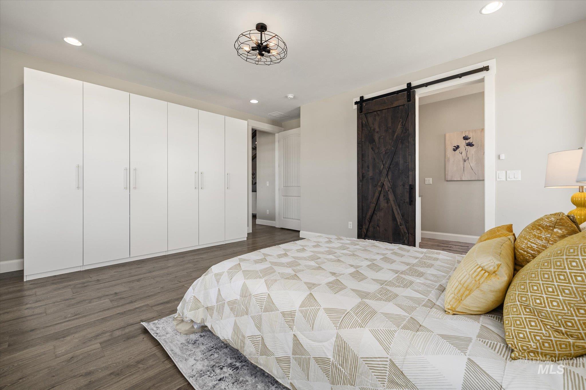 Bedroom featuring a barn door, dark wood-style flooring, and recessed lighting