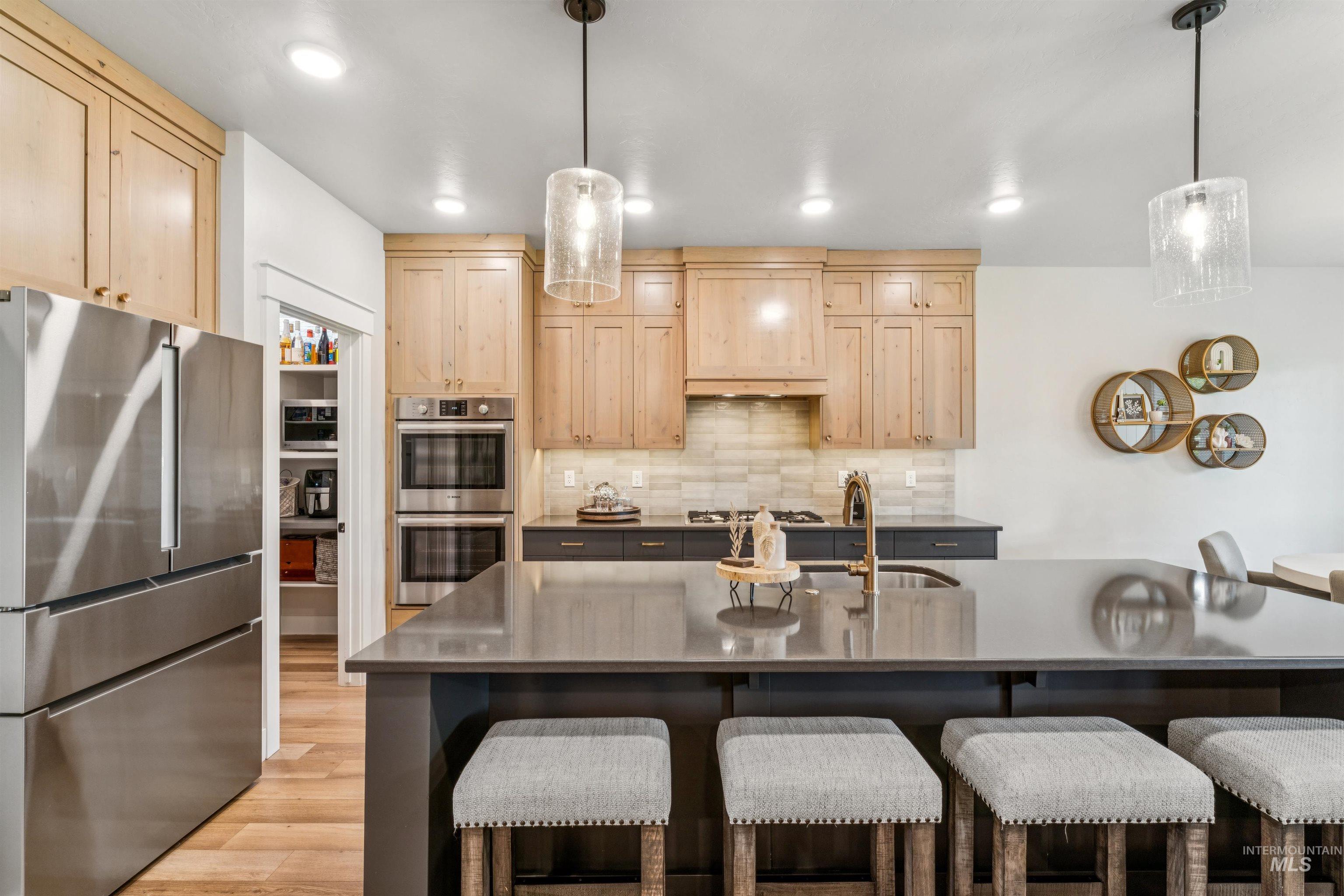Kitchen featuring appliances with stainless steel finishes, light brown cabinets, decorative backsplash, a center island with sink, and light wood finished floors