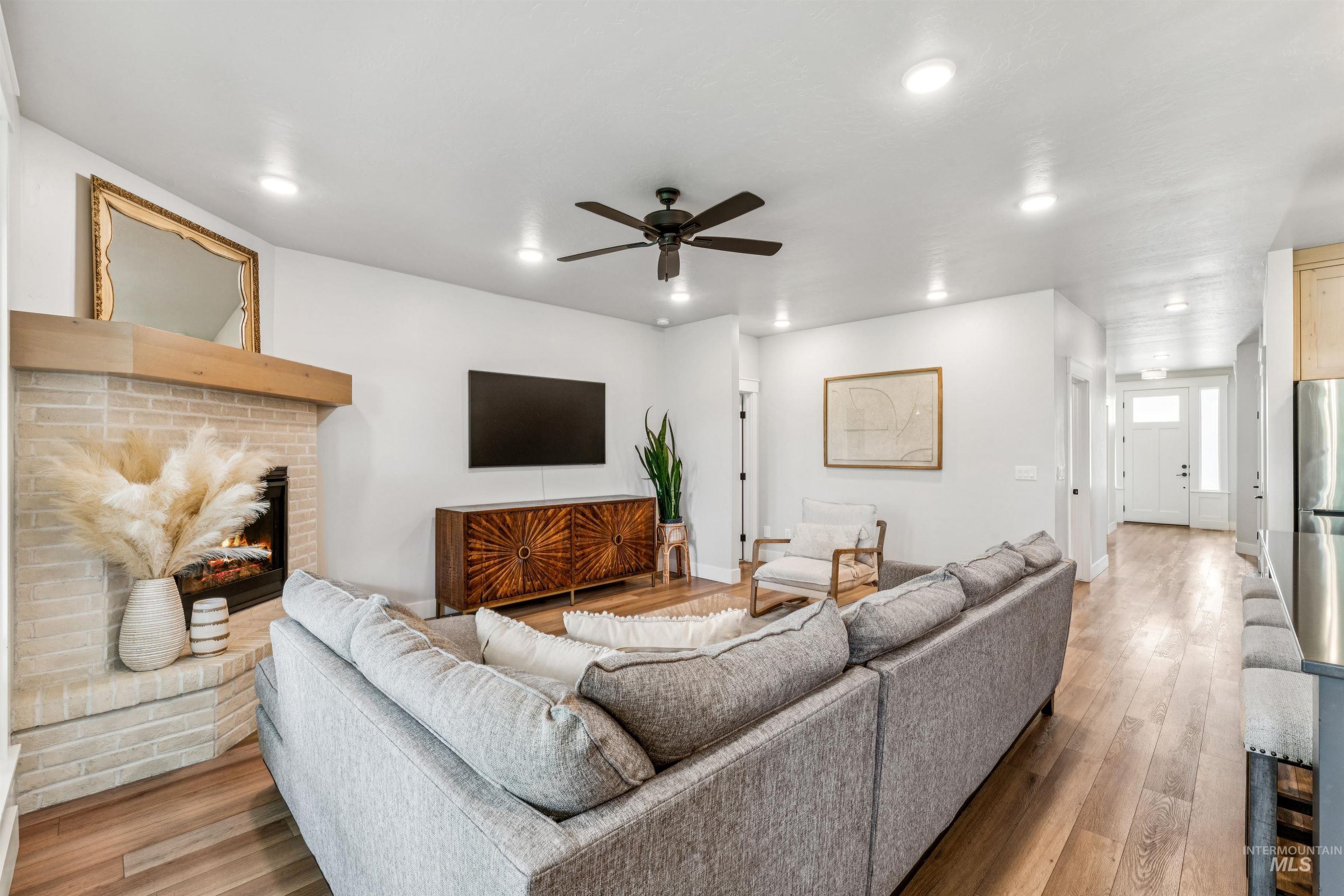 Living room with wood finished floors, a brick fireplace, a ceiling fan, and recessed lighting