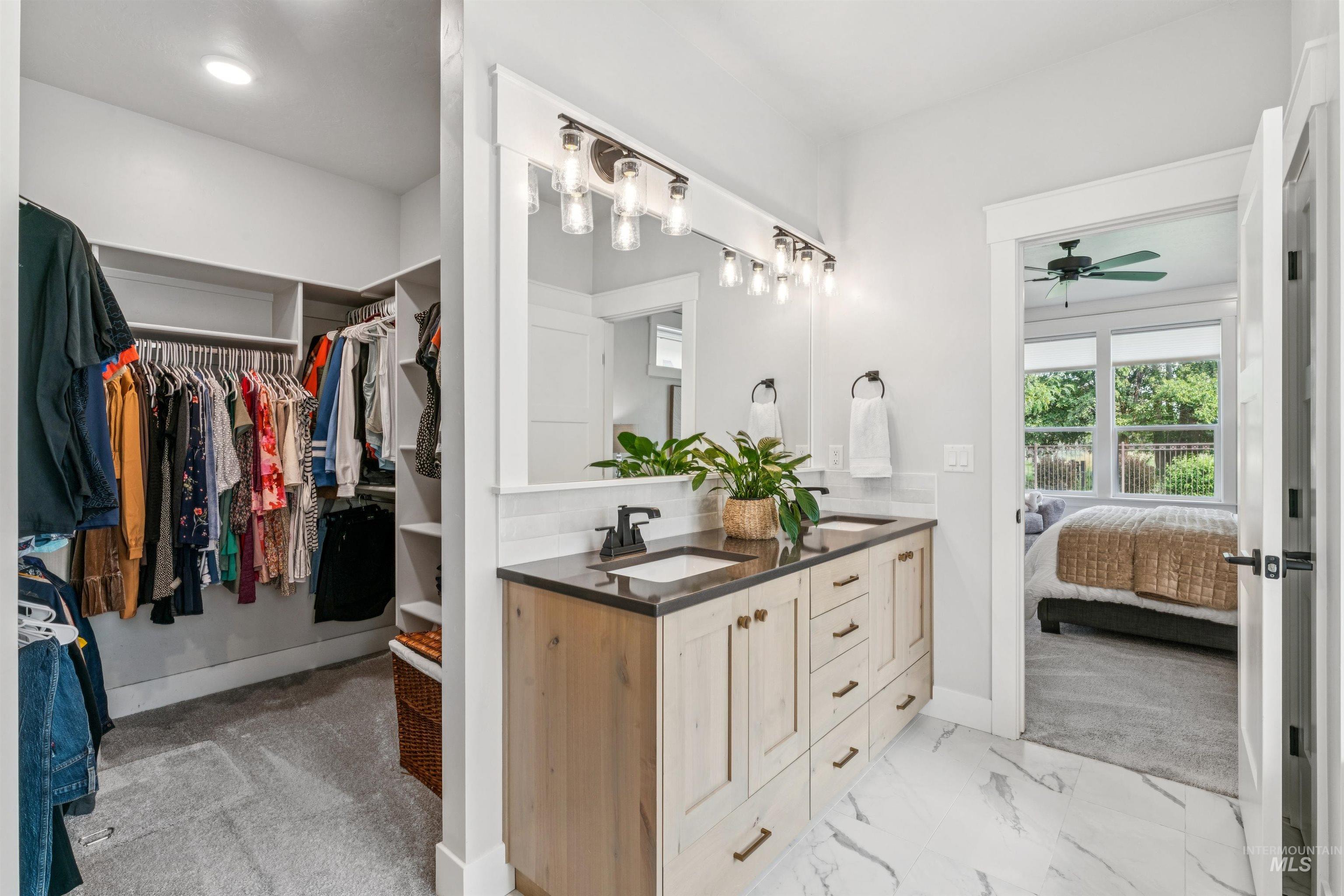 Ensuite bathroom featuring double vanity, a spacious closet, light marble finish floors, and a ceiling fan