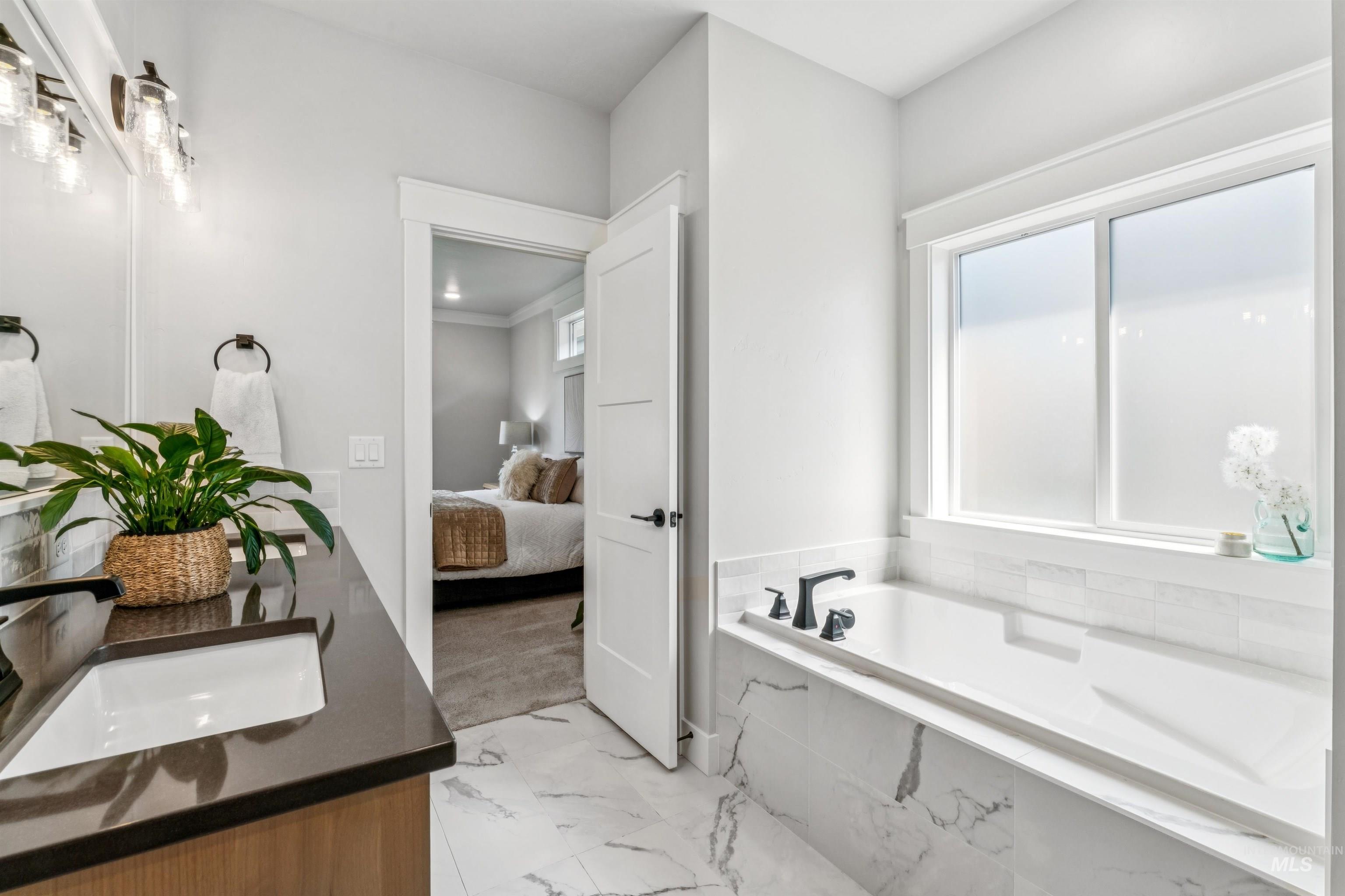 Ensuite bathroom with a garden tub, double vanity, and light marble finish floors