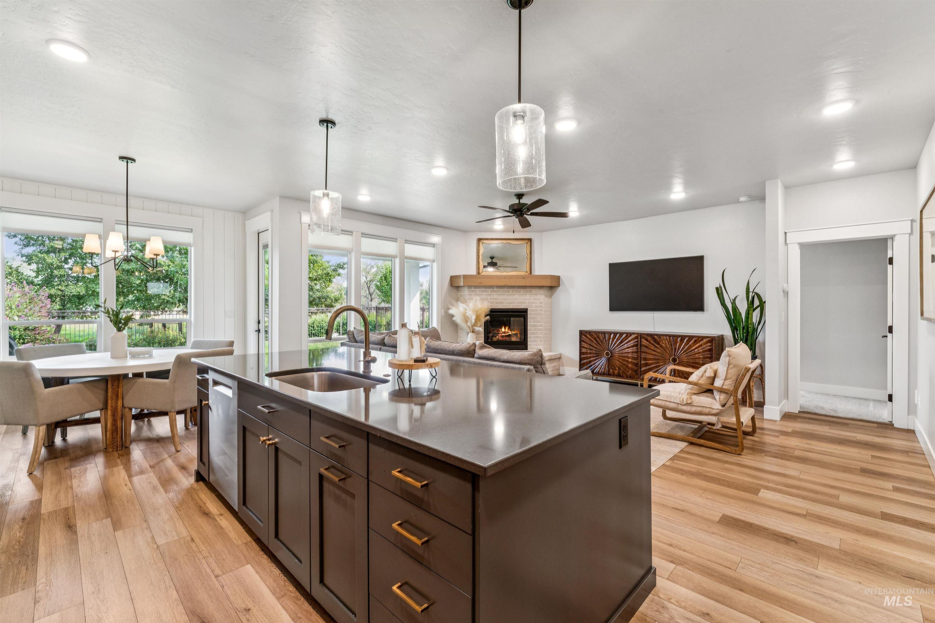 Kitchen with a glass covered fireplace, open floor plan, pendant lighting, light wood finished floors, and an island with sink
