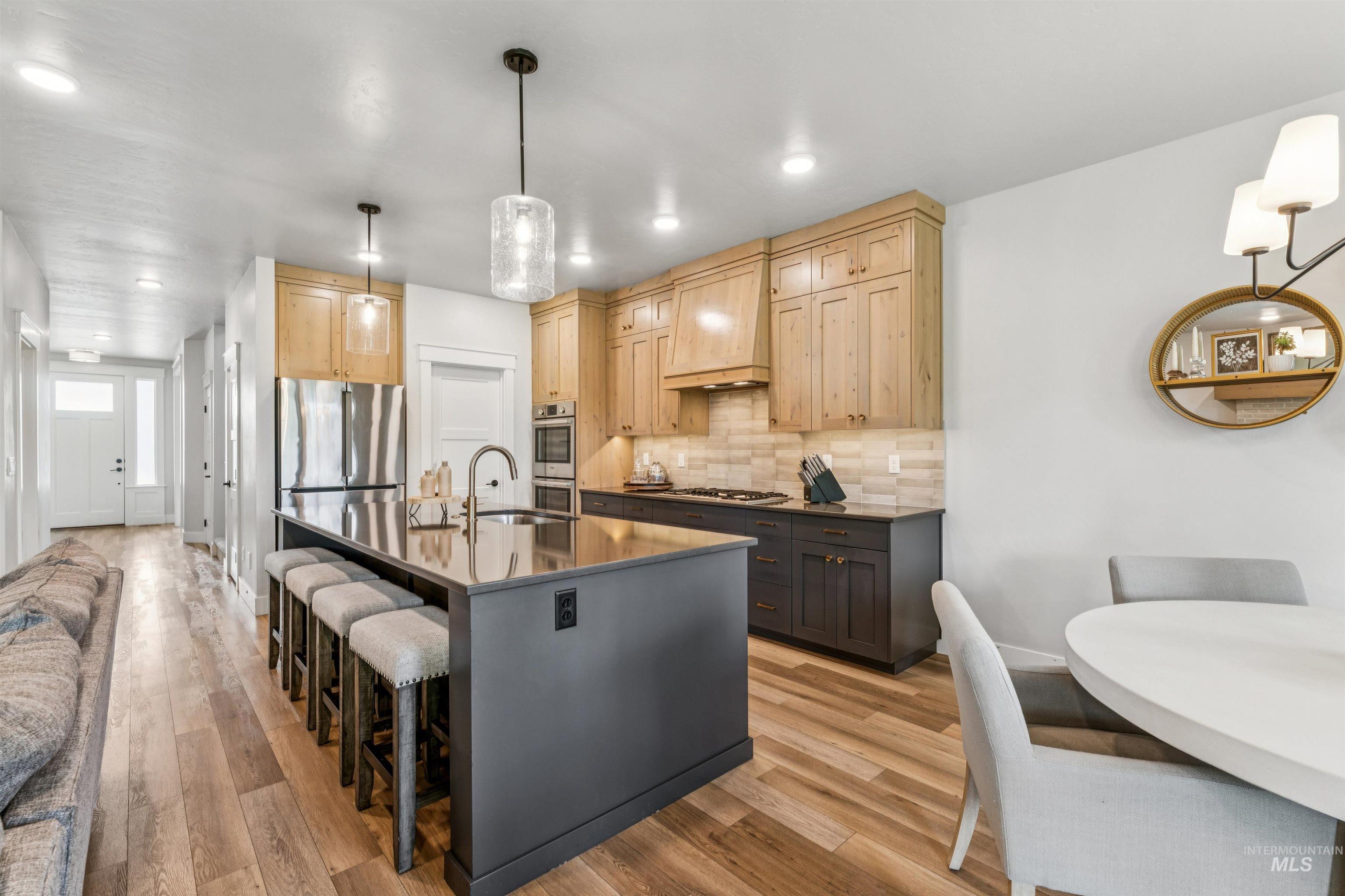 Kitchen with decorative backsplash, light wood-style floors, a kitchen bar, light brown cabinetry, and an island with sink