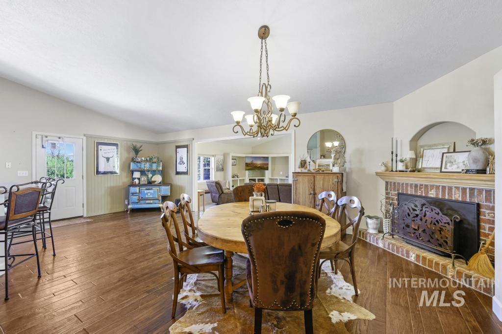 Dining room with a brick fireplace, lofted ceiling, a chandelier, dark wood-style flooring, and plenty of natural light