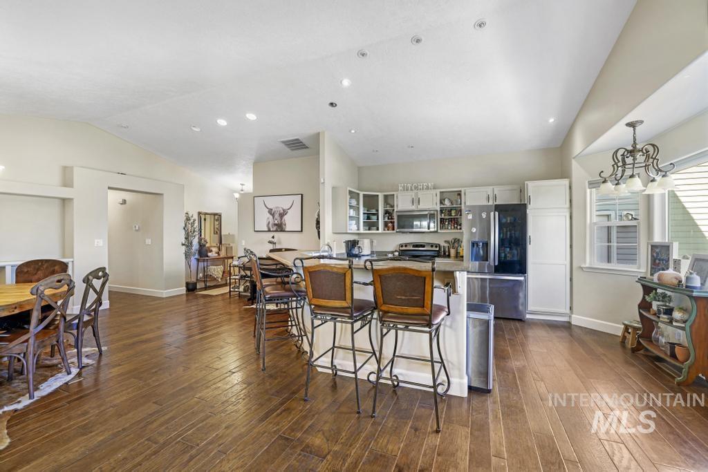 Kitchen featuring a kitchen breakfast bar, stainless steel appliances, glass insert cabinets, white cabinetry, and dark wood finished floors