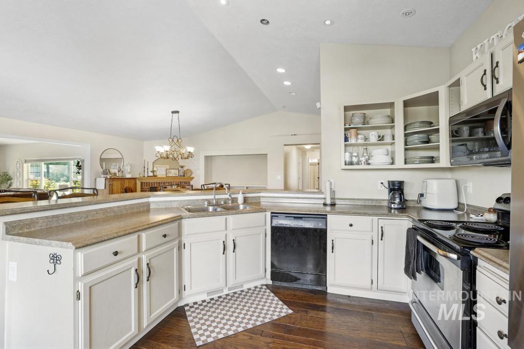 Kitchen featuring appliances with stainless steel finishes, white cabinetry, lofted ceiling, dark wood-style flooring, and a peninsula