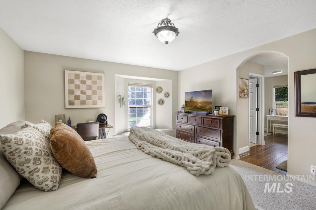 Bedroom with arched walkways, wood finished floors, and a textured ceiling