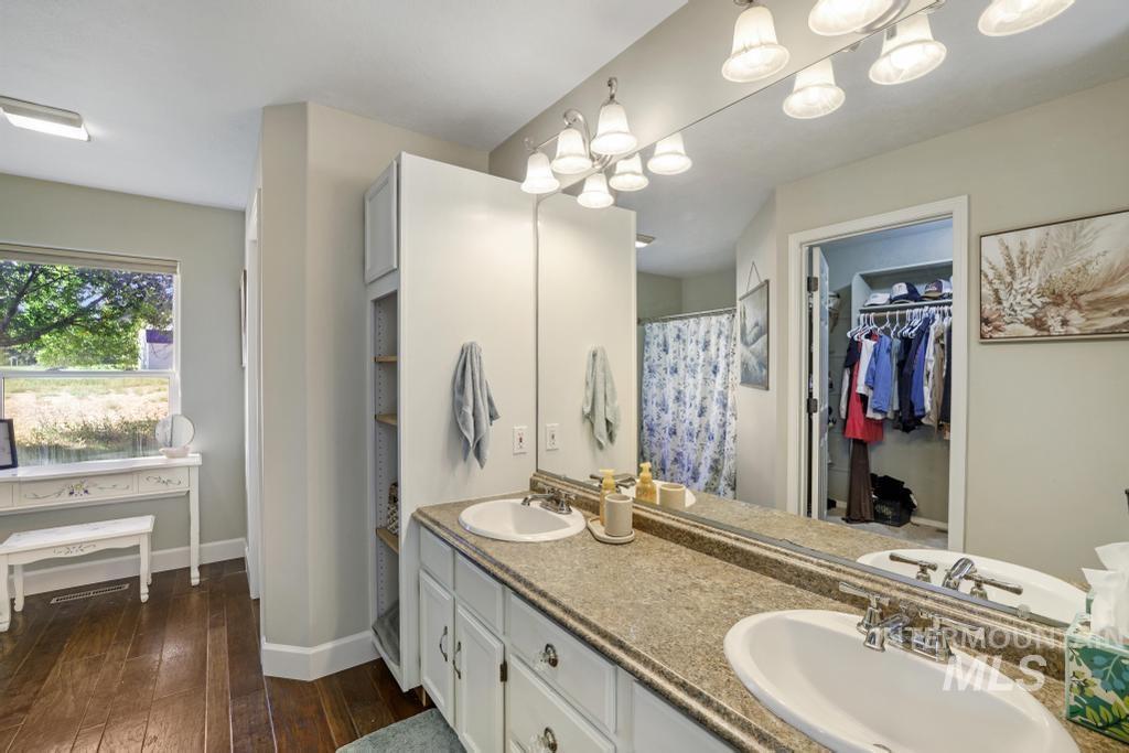 Full bathroom featuring double vanity, dark wood-style flooring, a walk in closet, a shower with curtain, and a chandelier