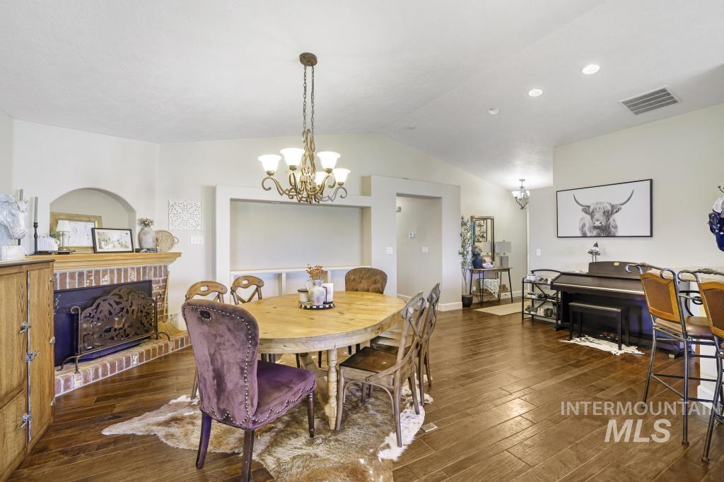 Dining room with lofted ceiling, dark wood-style flooring, a chandelier, a fireplace, and recessed lighting