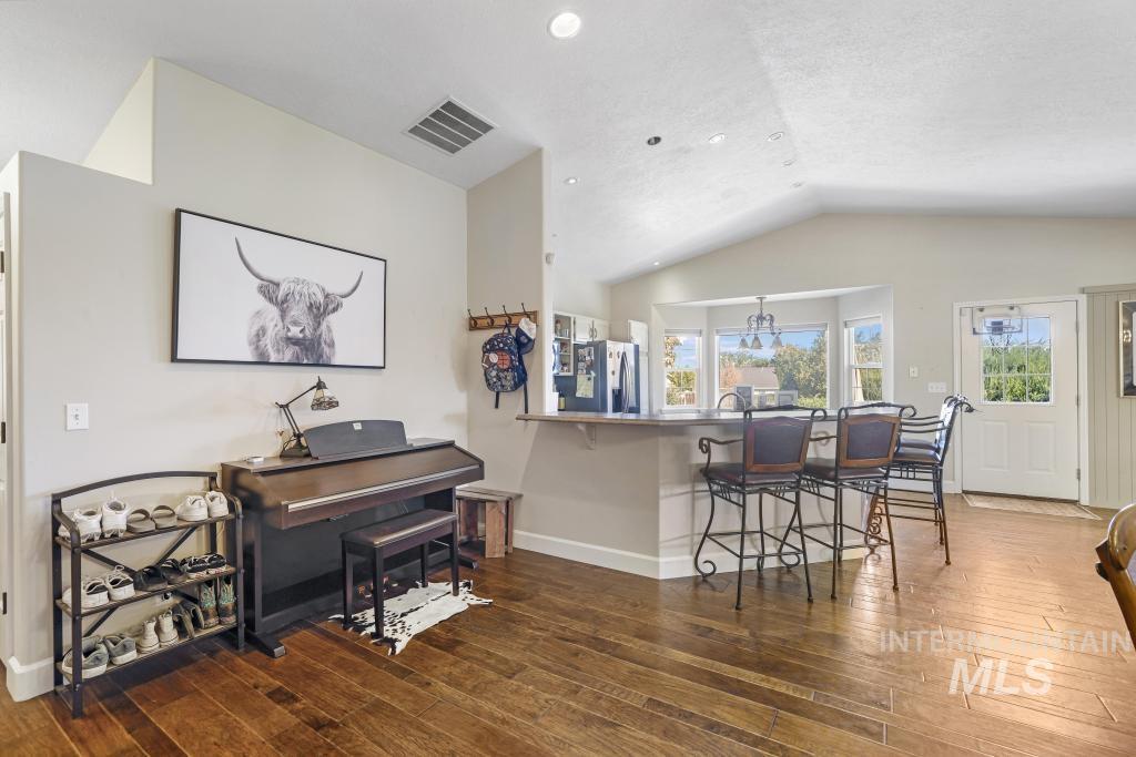 Kitchen with a kitchen bar, lofted ceiling, a peninsula, dark wood-style floors, and stainless steel fridge with ice dispenser