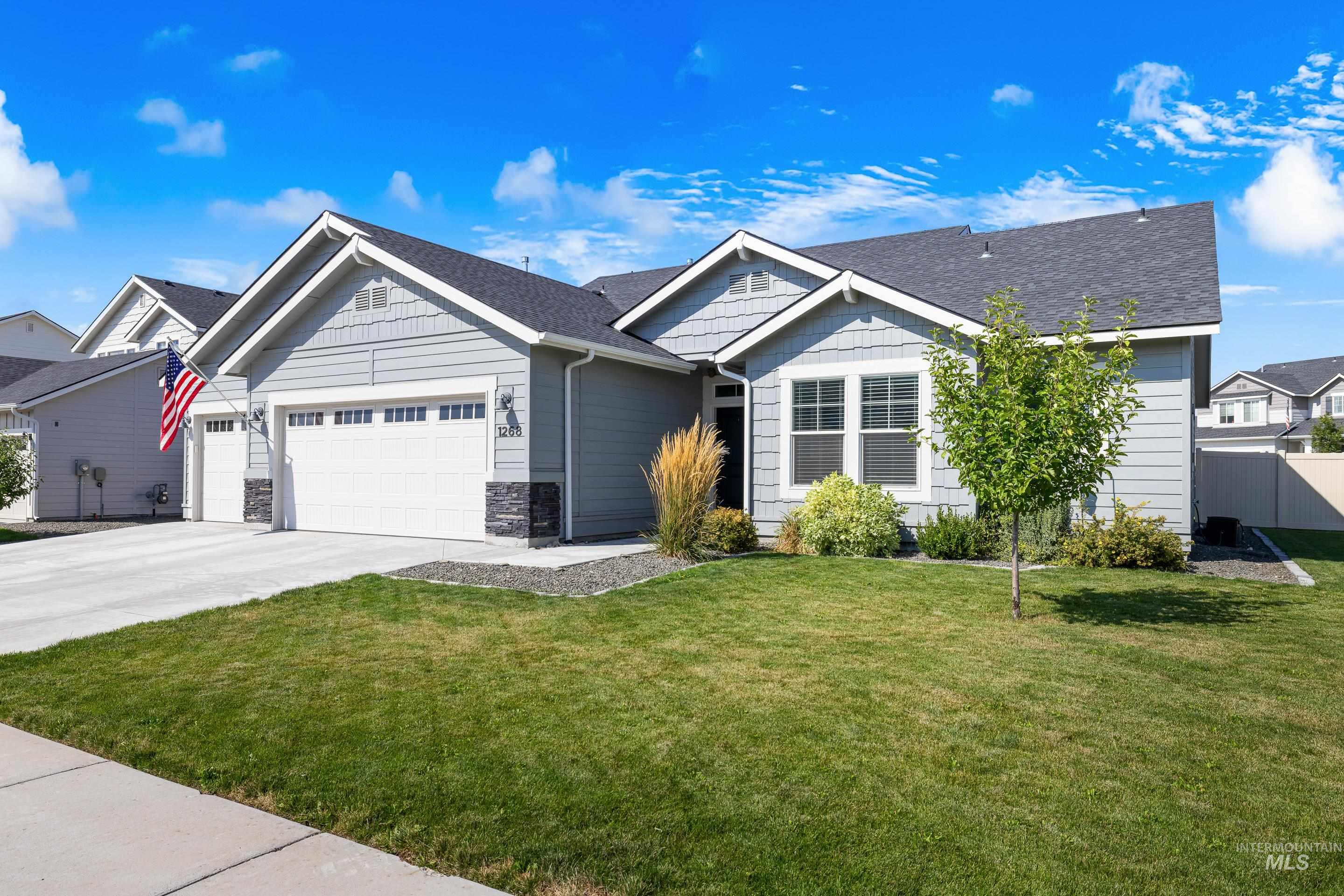 View of front facade with a front yard, driveway, an attached garage, a shingled roof, and stone siding
