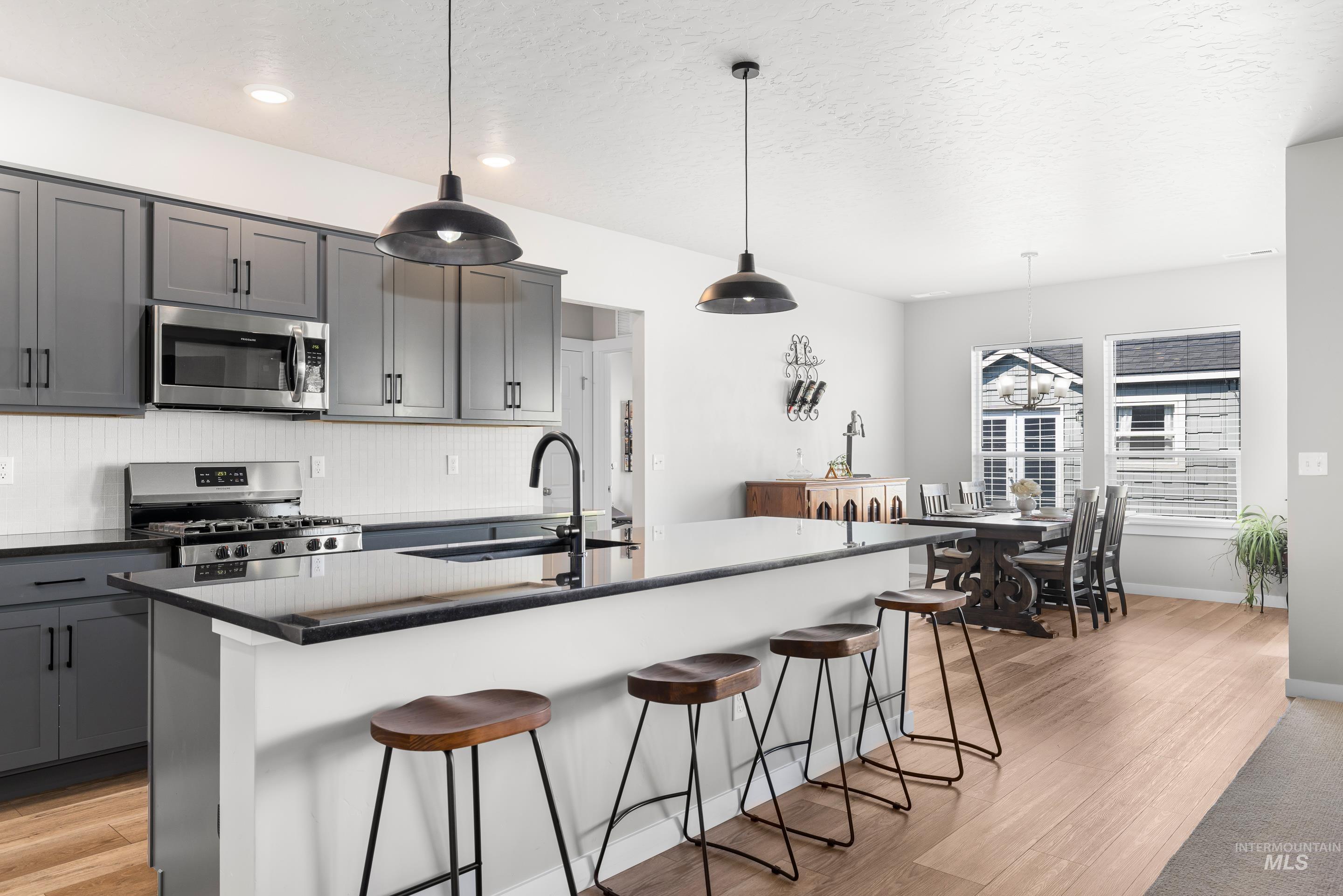 Kitchen with gray cabinets, light wood-type flooring, stainless steel appliances, a center island with sink, and pendant lighting