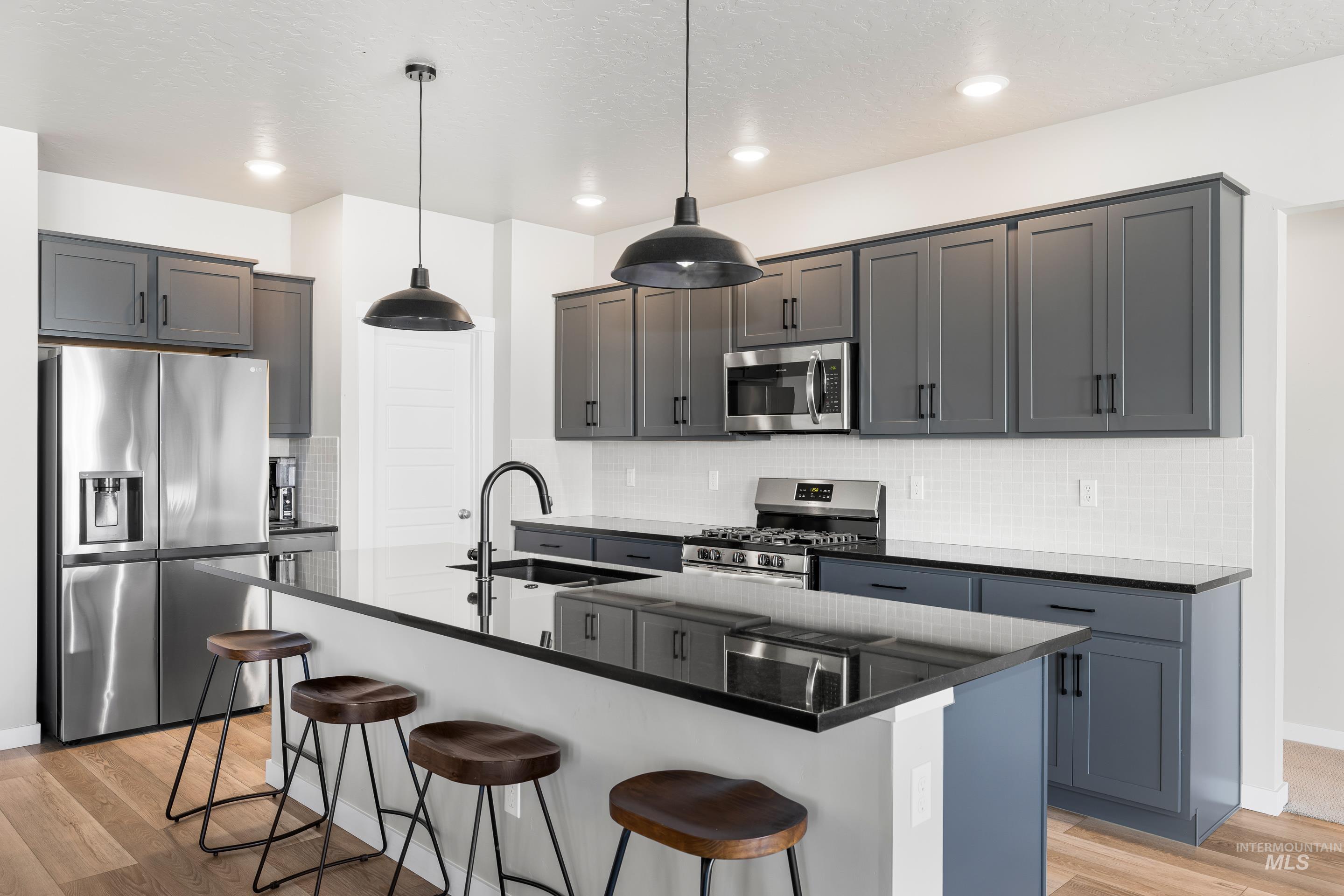 Kitchen with an island with sink, stainless steel appliances, light wood-type flooring, a kitchen bar, and pendant lighting