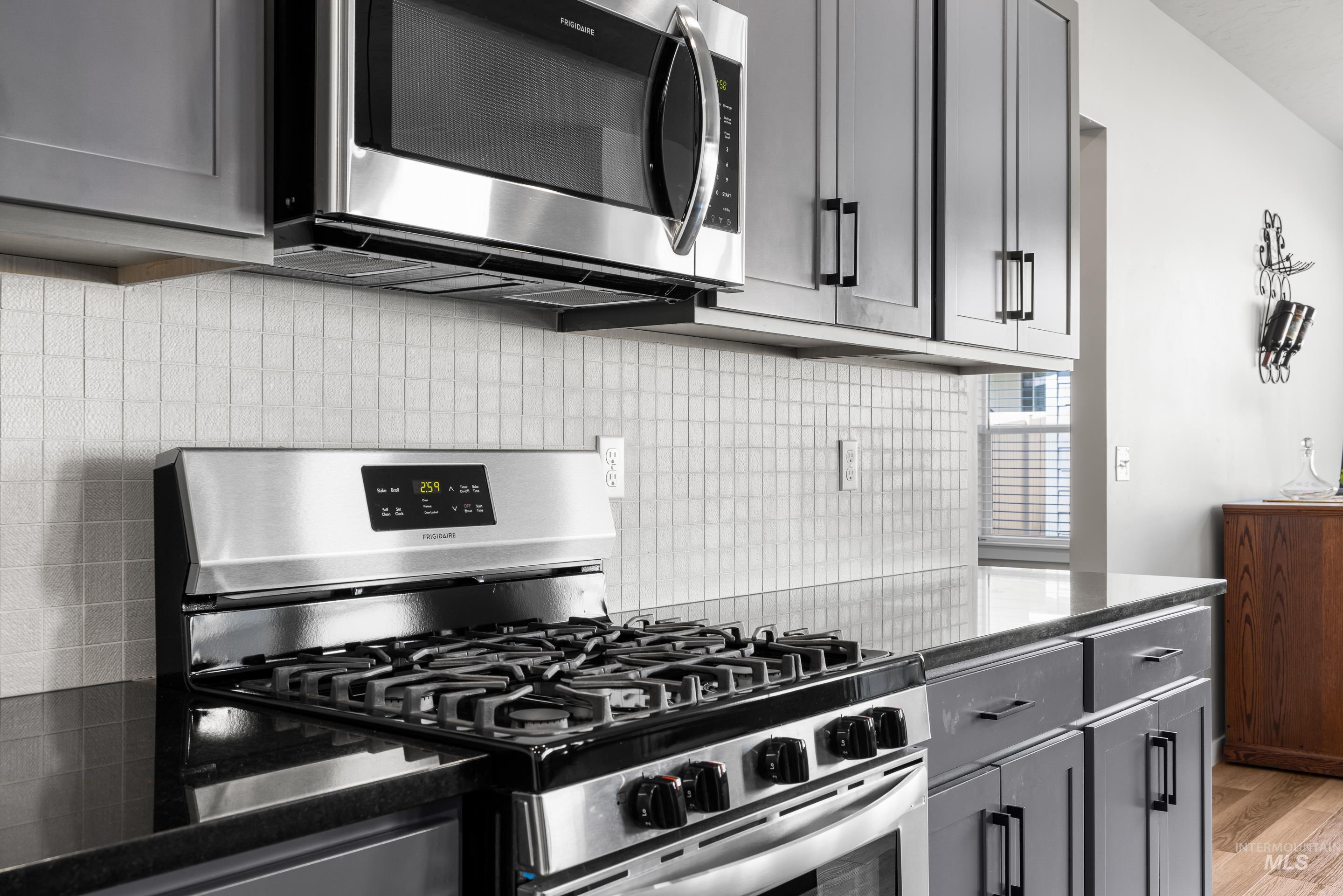 Kitchen with stainless steel appliances, gray cabinets, tasteful backsplash, light wood finished floors, and dark stone countertops