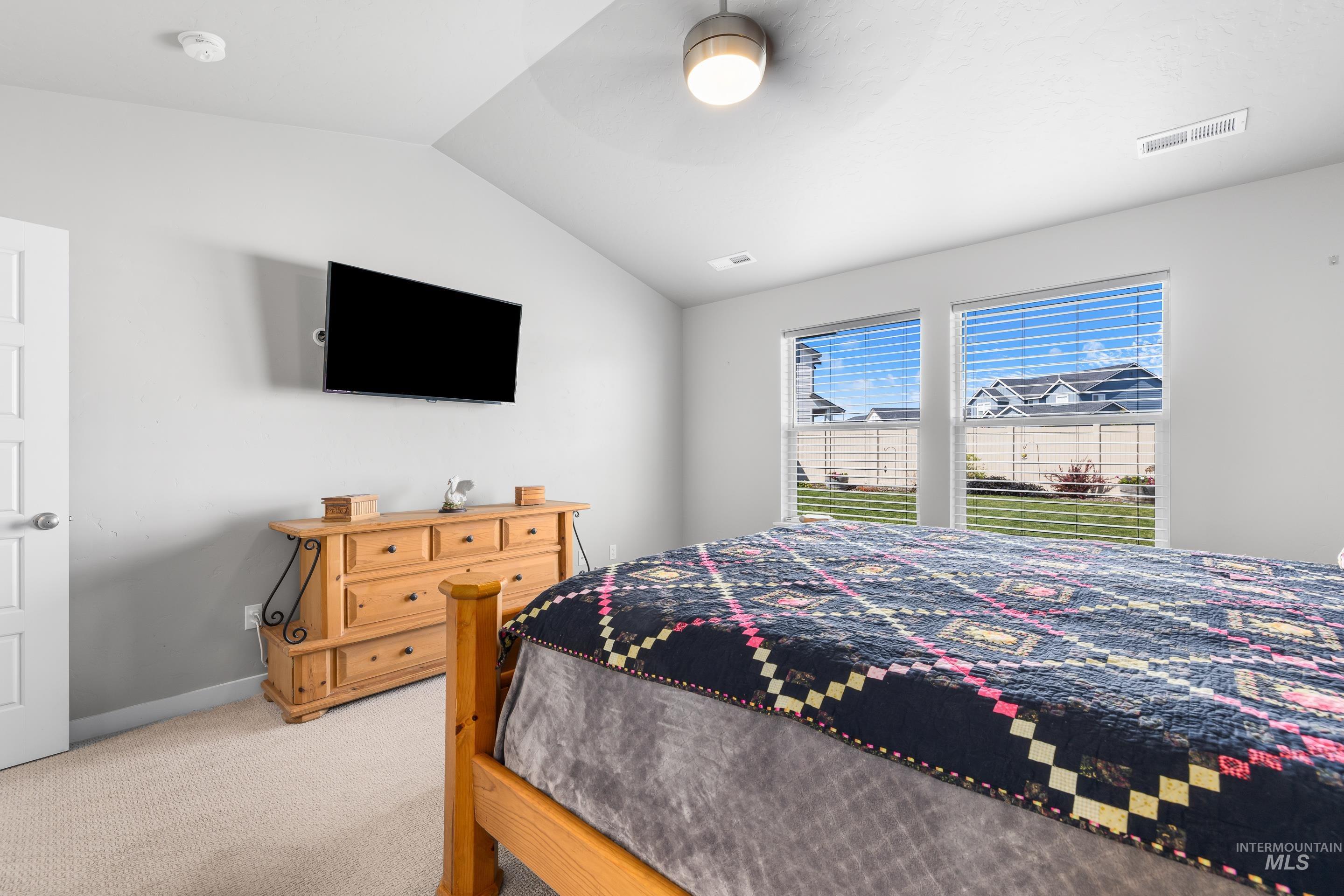 Carpeted bedroom featuring vaulted ceiling and ceiling fan