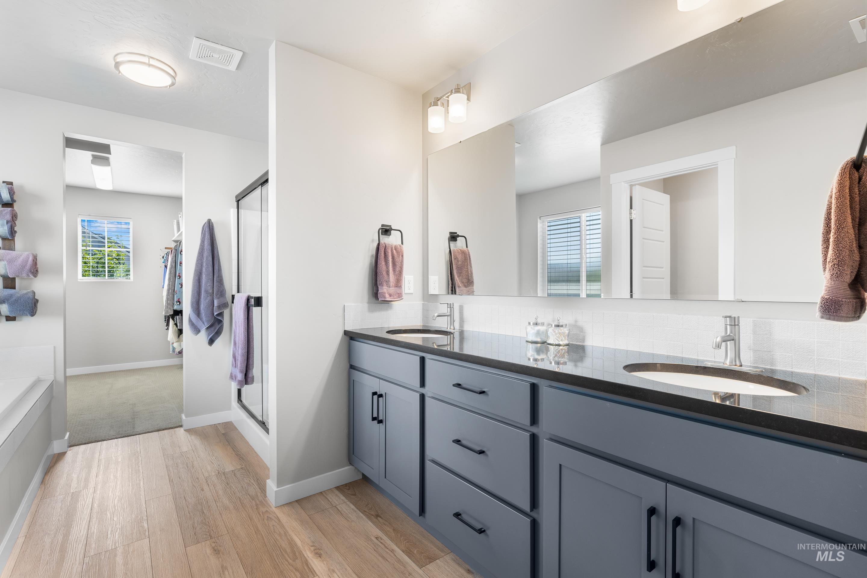 Bathroom with double vanity, light wood-style flooring, plenty of natural light, and a stall shower