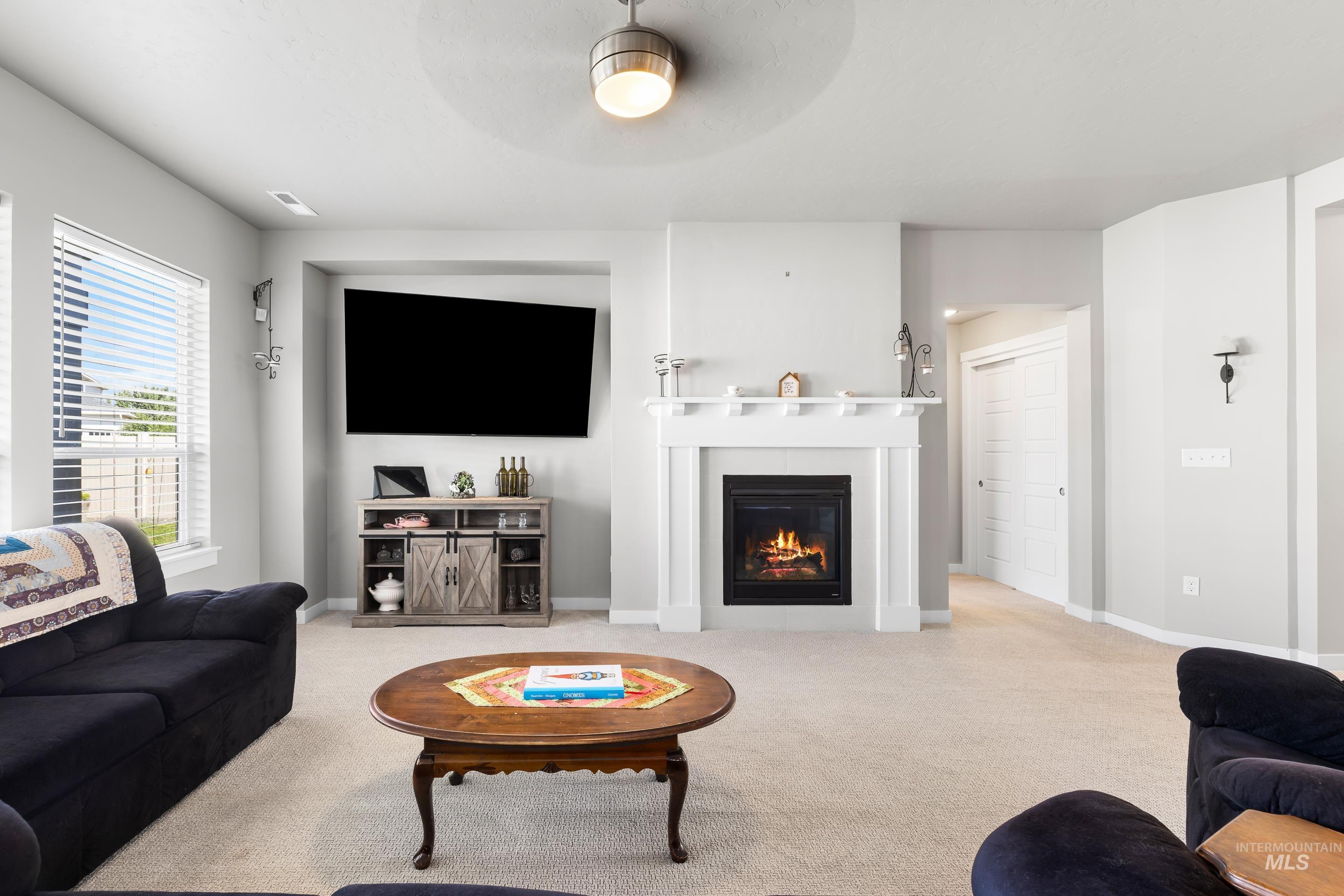 Carpeted living area featuring a glass covered fireplace and baseboards