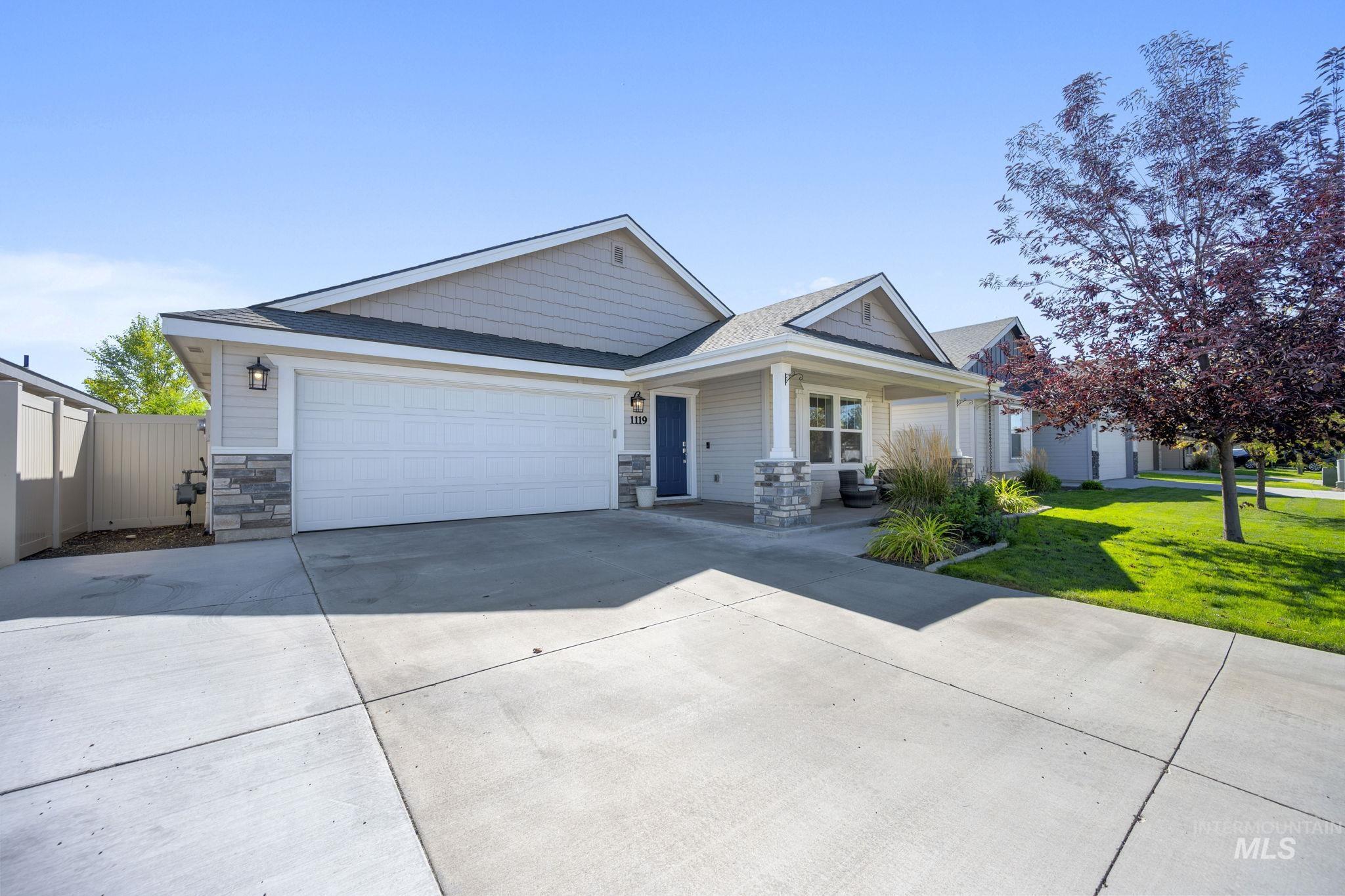 View of front of property with driveway, stone siding, a front yard, a shingled roof, and a porch