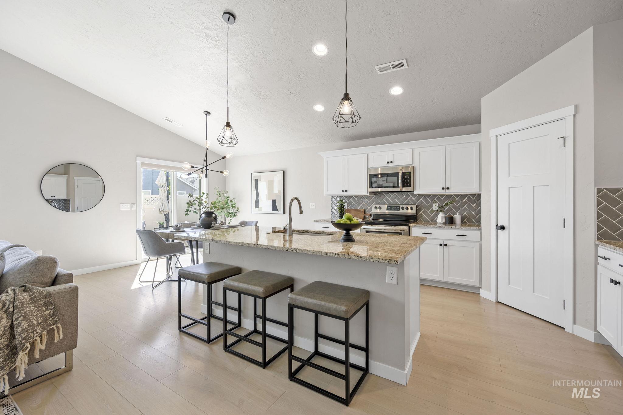 Kitchen featuring backsplash, a center island with sink, a kitchen bar, light stone counters, and white cabinets