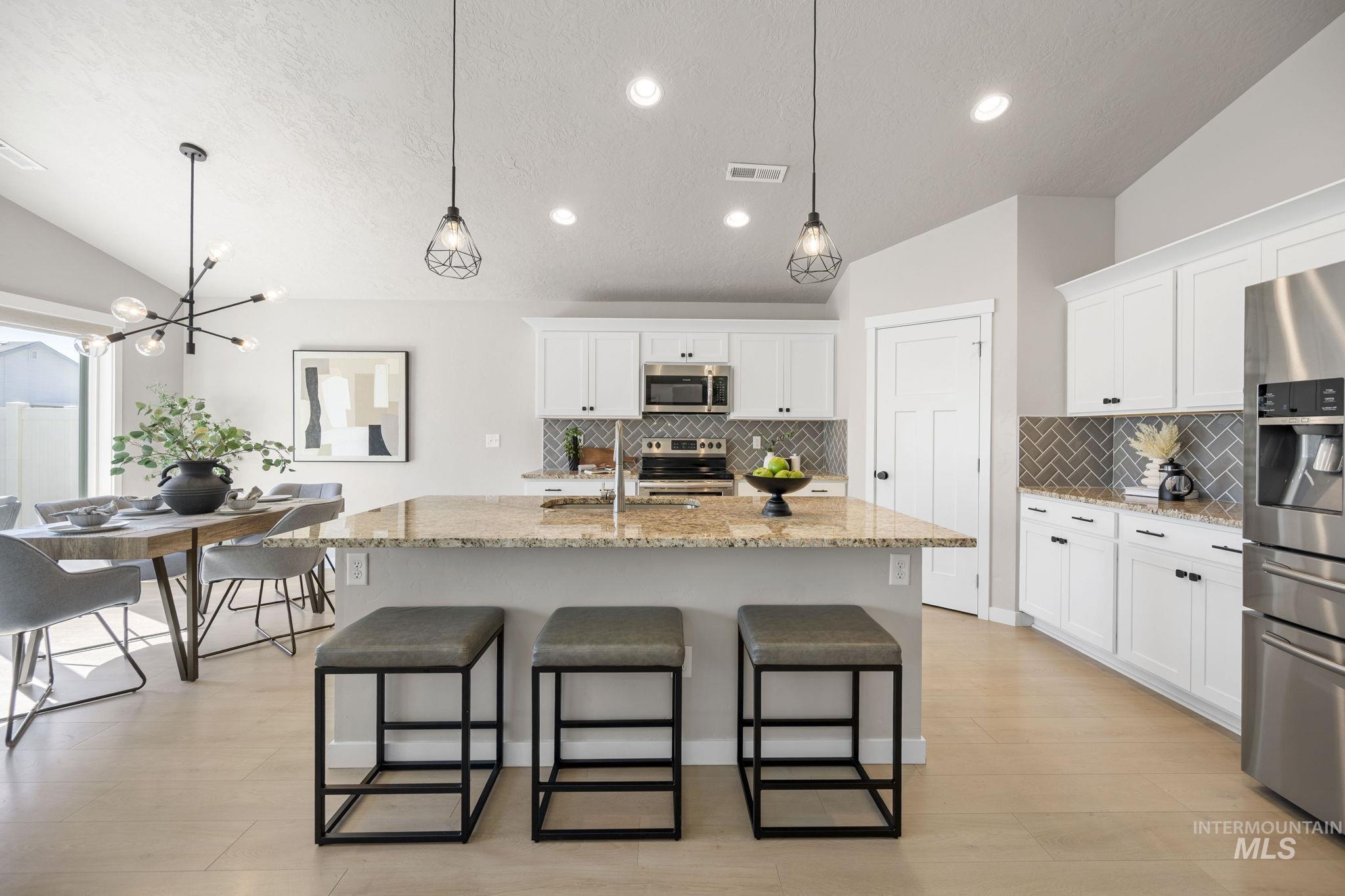 Kitchen with vaulted ceiling, hanging light fixtures, white cabinetry, light stone countertops, and a textured ceiling