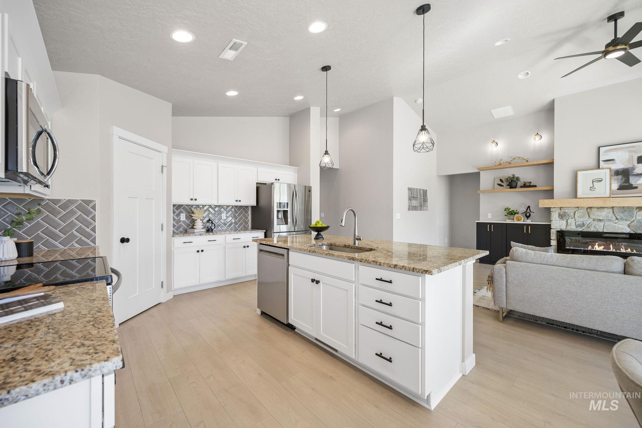 Kitchen featuring open floor plan, a center island with sink, light stone counters, hanging light fixtures, and white cabinetry