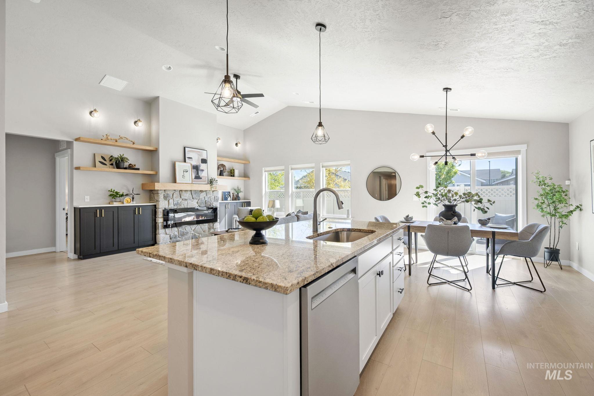 Kitchen featuring light stone counters, stainless steel dishwasher, hanging light fixtures, a kitchen island with sink, and a ceiling fan