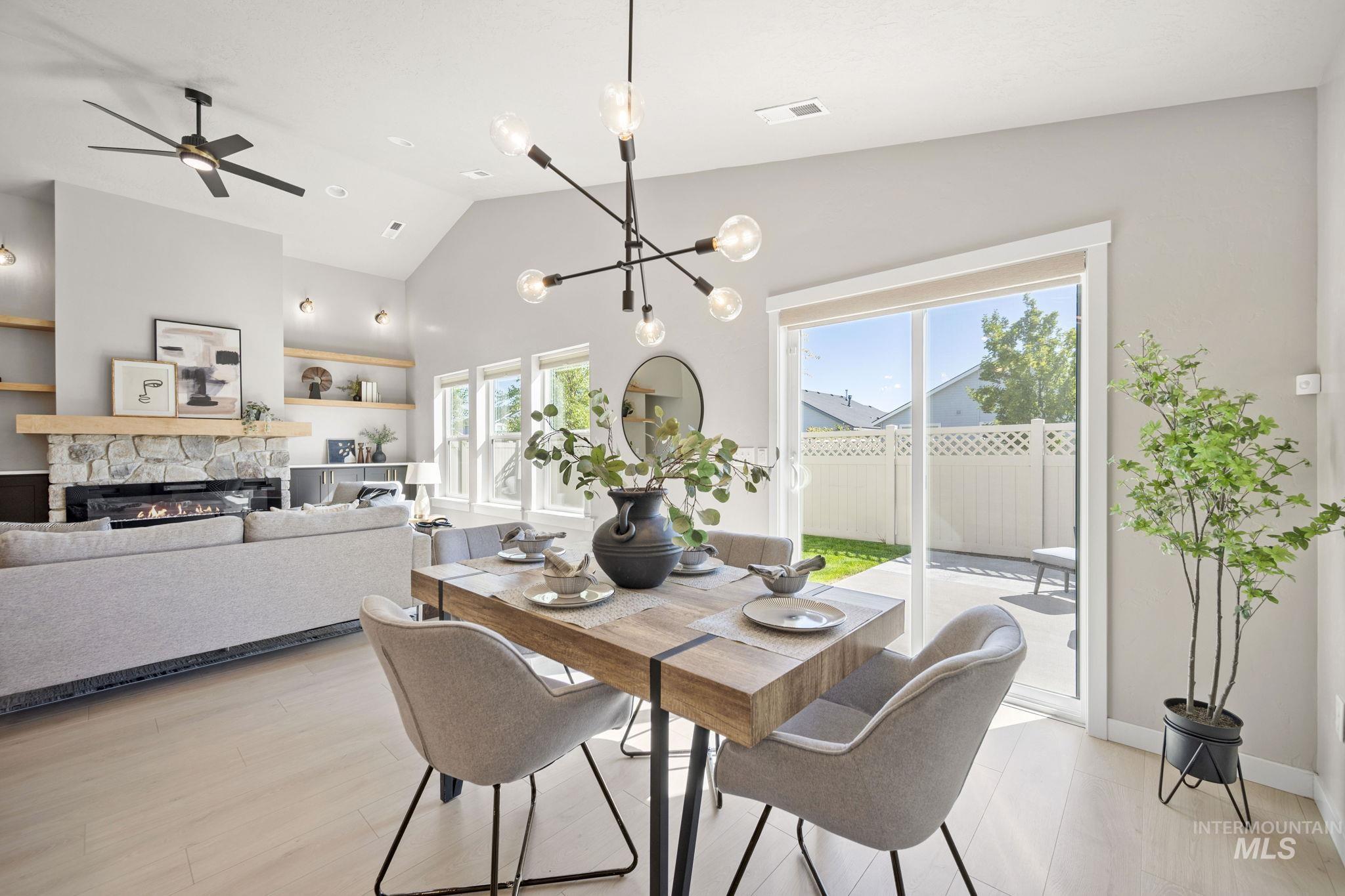 Dining room featuring a fireplace, a chandelier, high vaulted ceiling, light wood-style flooring, and a ceiling fan