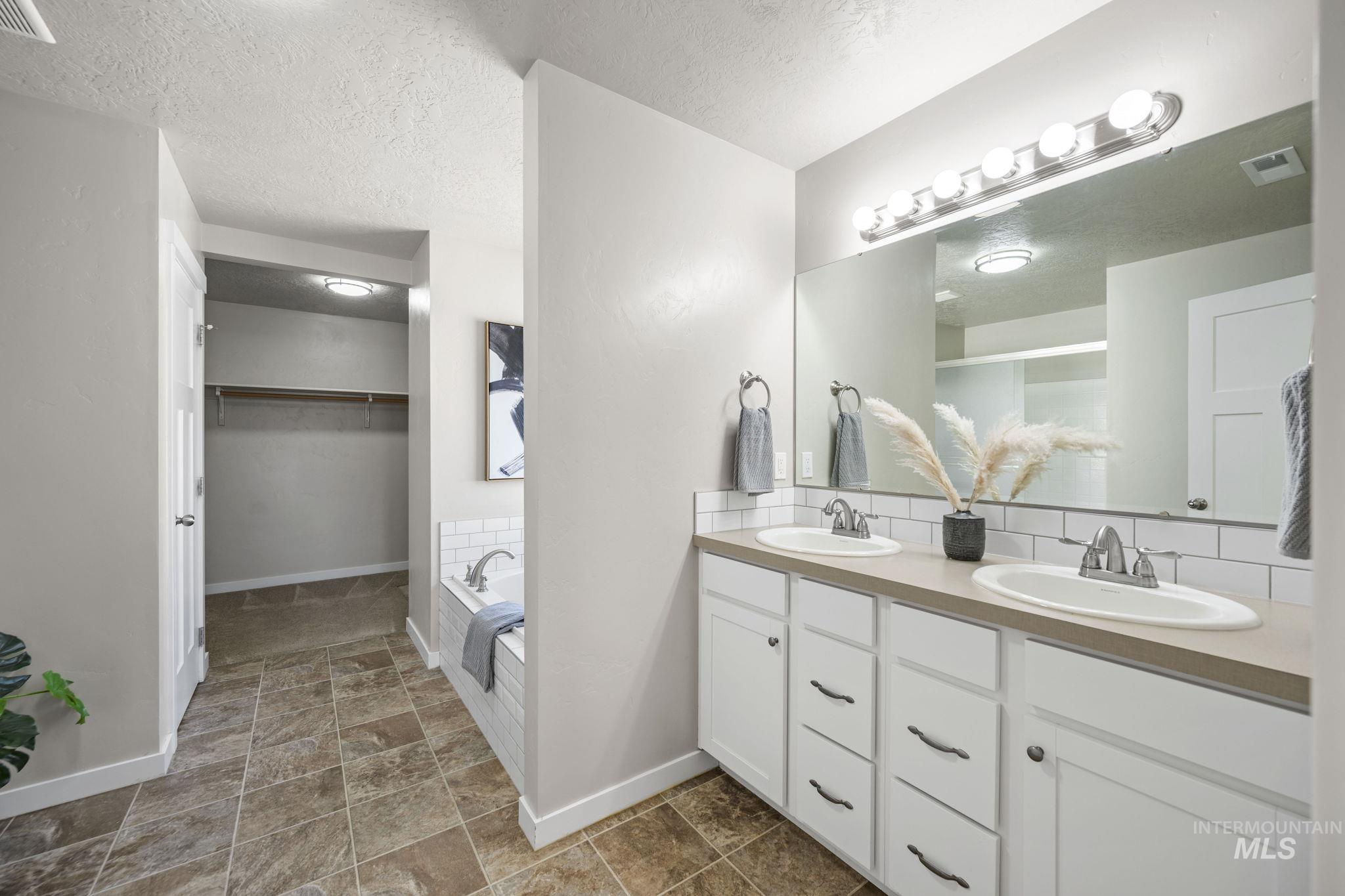 Full bathroom with double vanity, a textured ceiling, a garden tub, and a spacious closet